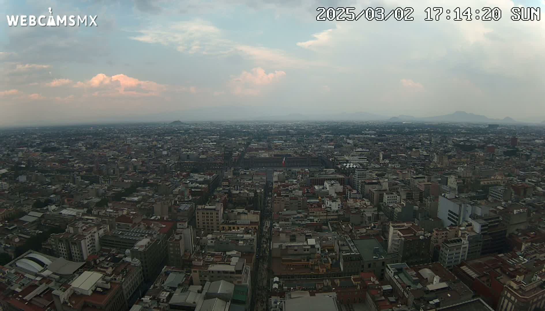 An expansive cityscape stretches to distant hazy mountains under a mostly cloudy sky.