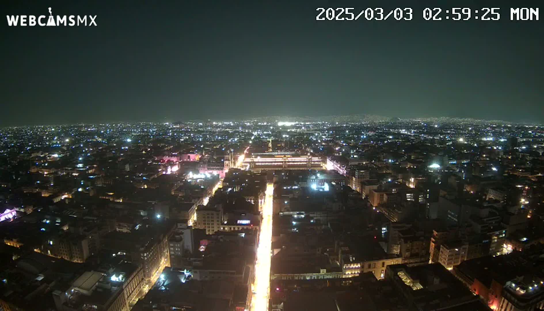 A nighttime aerial view shows a city illuminated by streetlights and building lights under a clear, dark sky.