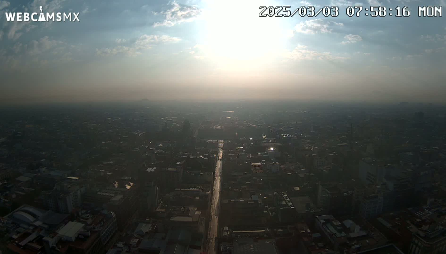 A hazy sunrise illuminates a sprawling cityscape, viewed from a high vantage point.