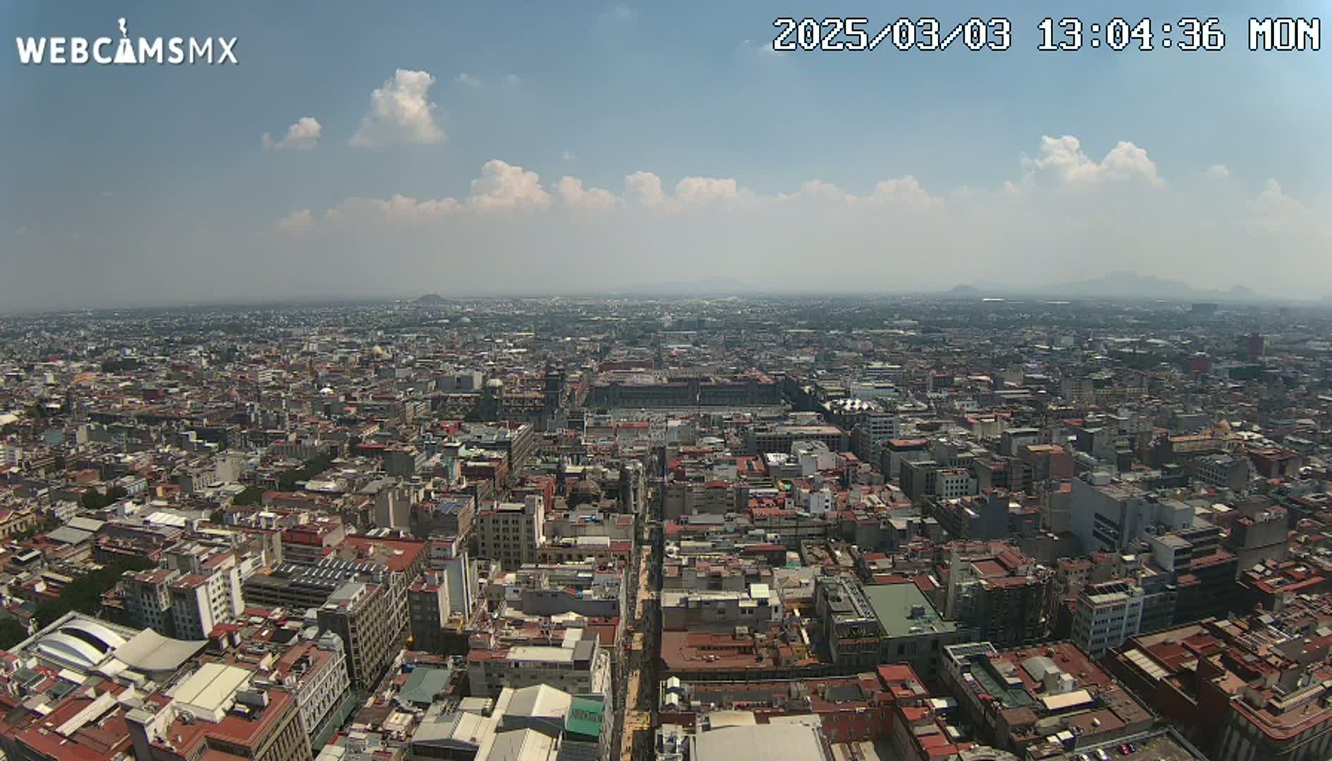 A high-angle, long shot shows a sprawling city under a partly cloudy sky.