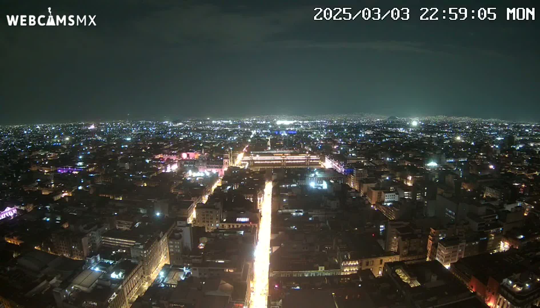 A nighttime aerial view of a sprawling city with brightly lit streets and buildings under a clear, dark sky.