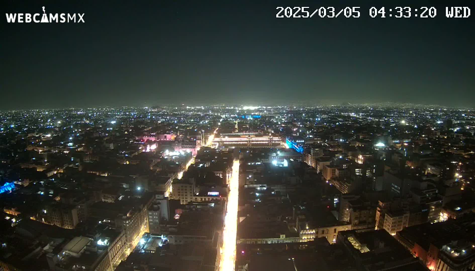 A nighttime aerial view of a sprawling city with brightly lit streets and buildings under a clear sky.