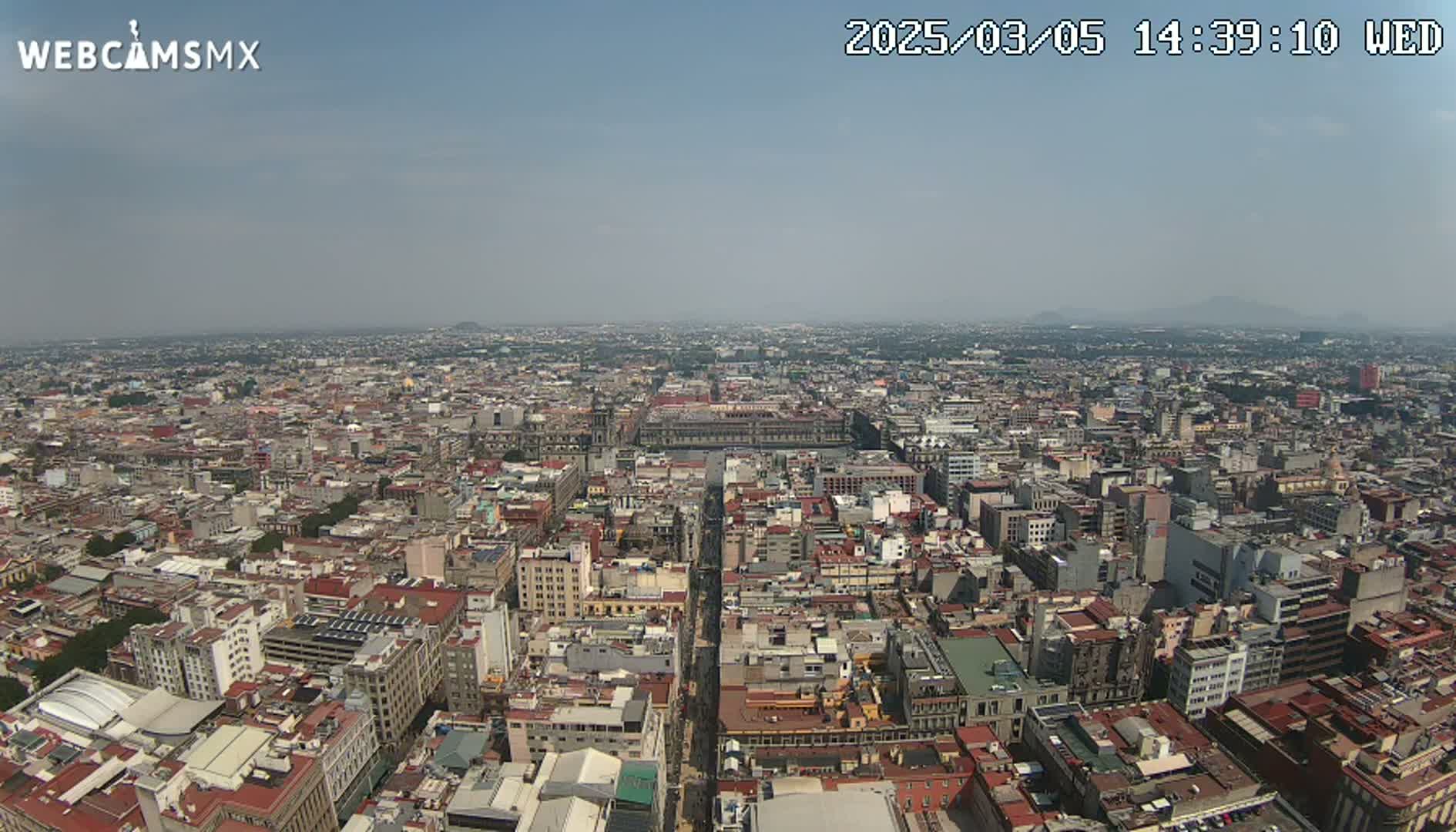 A hazy, sunny day overlooks a vast cityscape of densely packed buildings, stretching to the horizon with distant mountains visible.