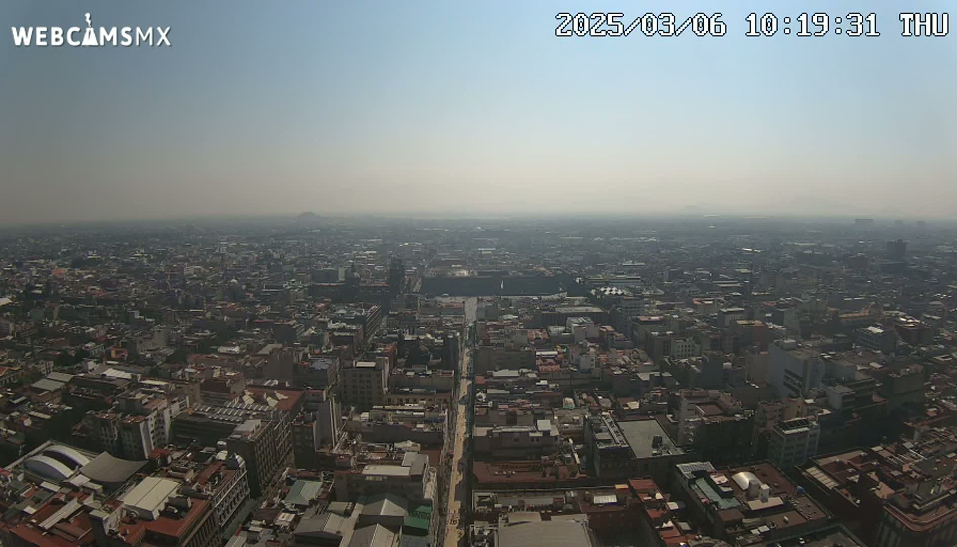 A hazy, sunny aerial view of a dense cityscape stretches to the horizon.