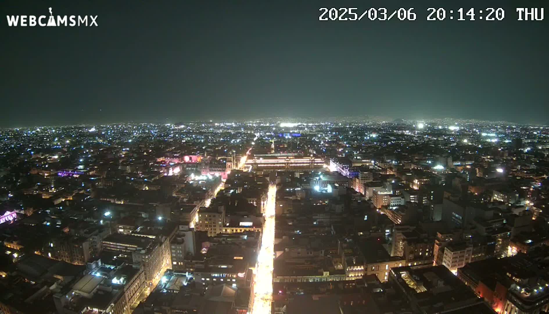 A brightly lit city at night is seen from a high vantage point under a clear, dark sky.