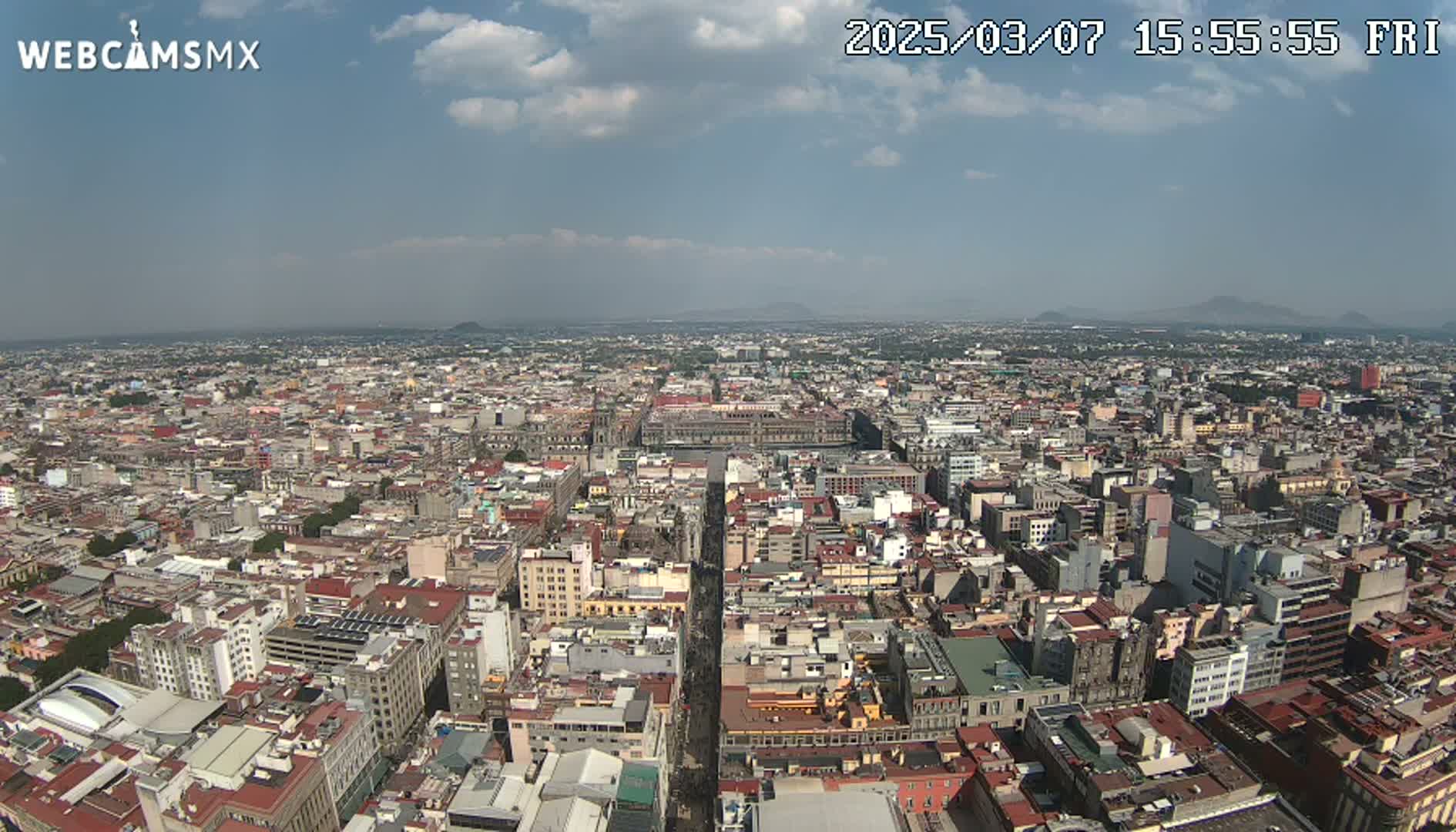 A high-angle, long shot of a sprawling city under a partly cloudy sky shows a dense collection of buildings extending to the horizon.