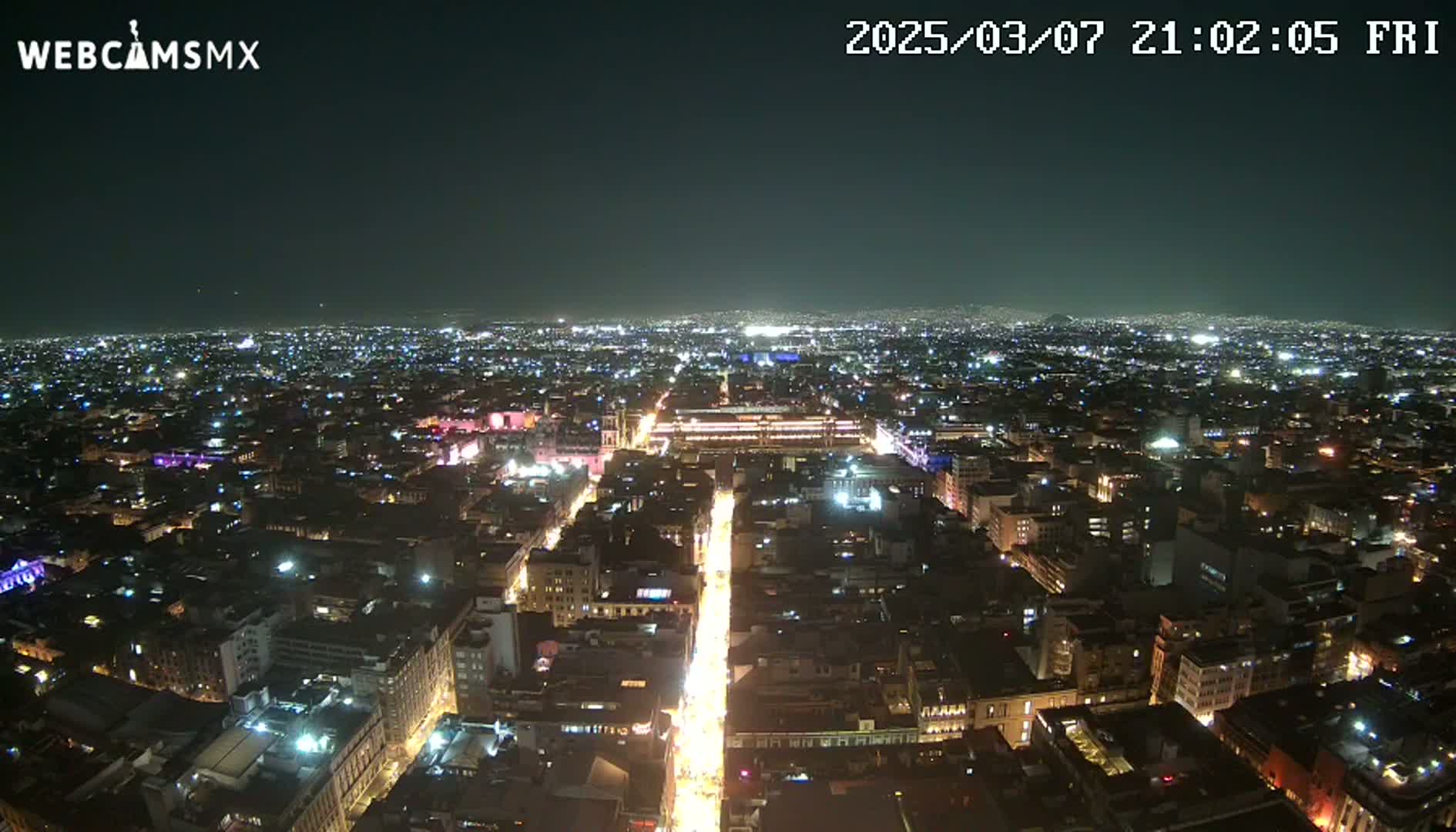 A nighttime aerial view of a sprawling city with brightly lit streets and buildings under a clear sky.