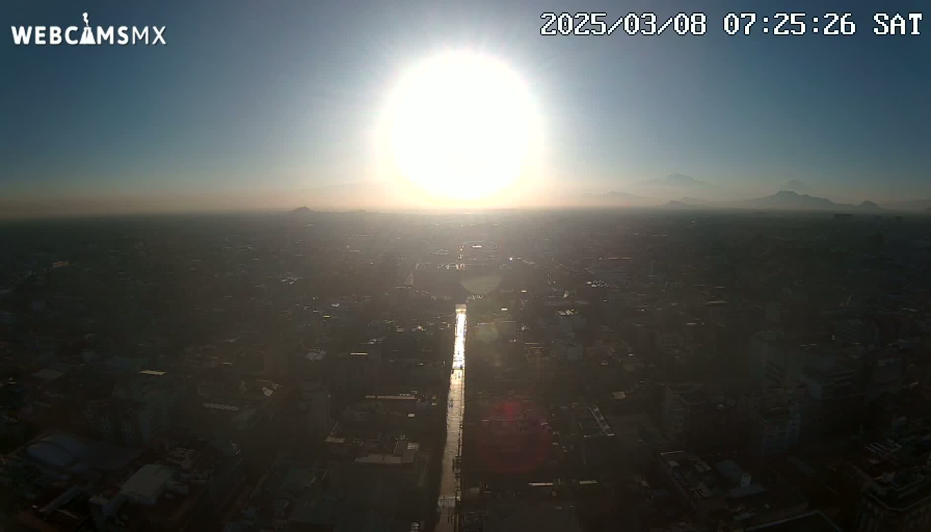 A hazy sunrise illuminates a sprawling city, with distant mountains visible on the horizon.