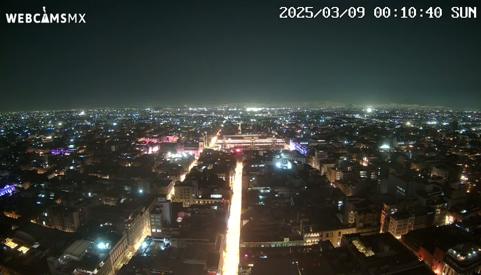 A nighttime, aerial view of a sprawling city with brightly lit streets and buildings under a clear sky.