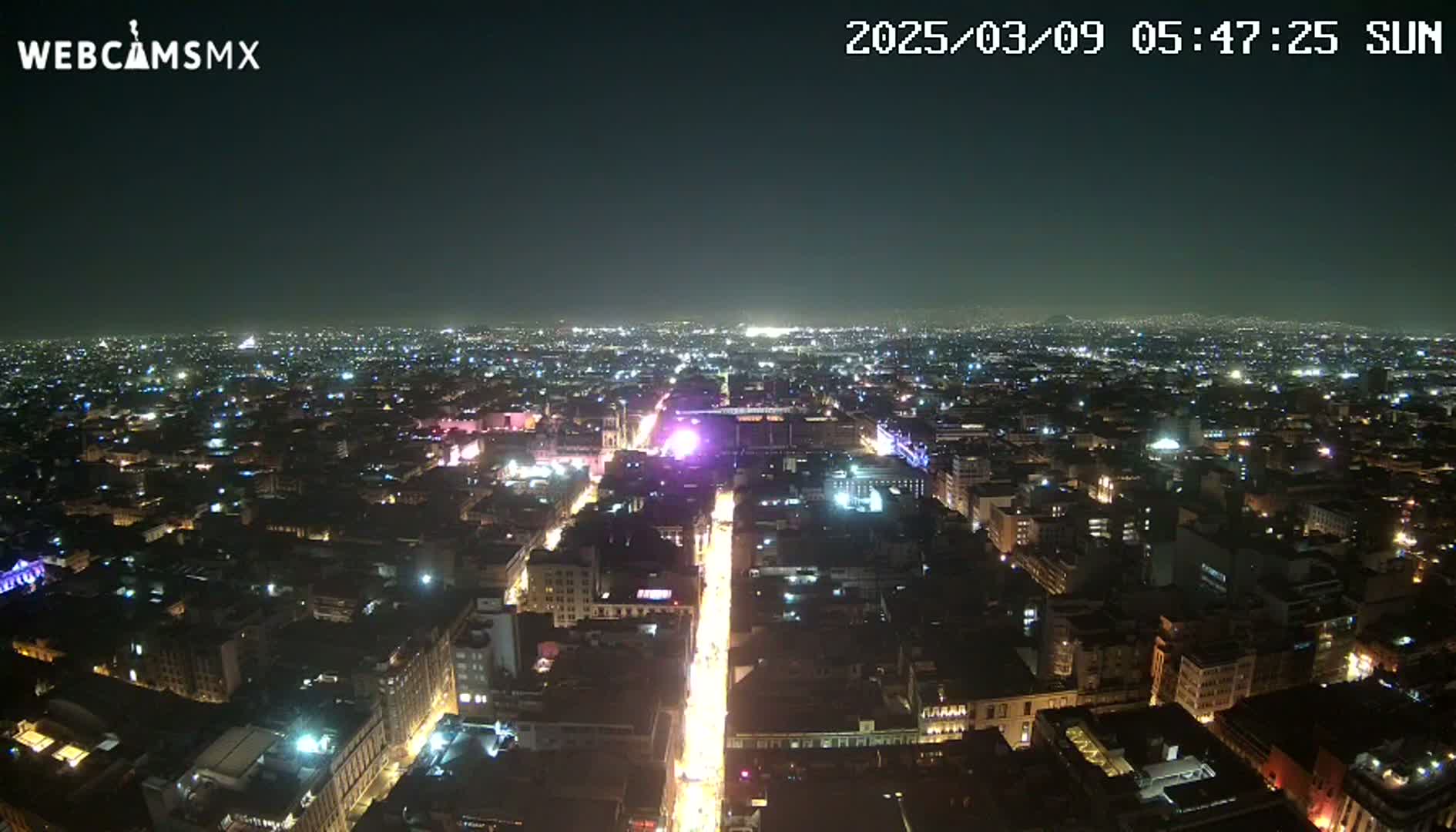 A nighttime aerial view of a city with brightly lit streets and buildings under a clear sky.