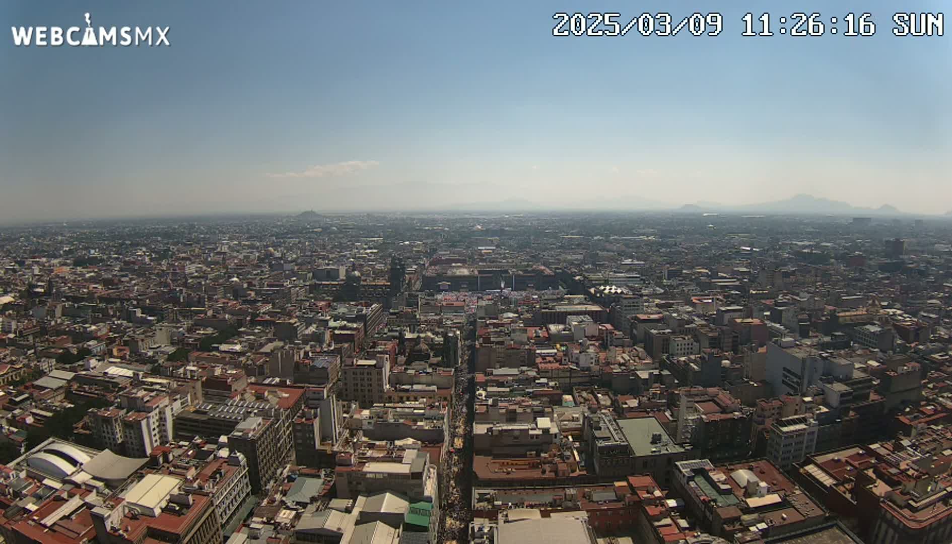 A hazy, sunny day reveals a sprawling cityscape extending to distant mountains.