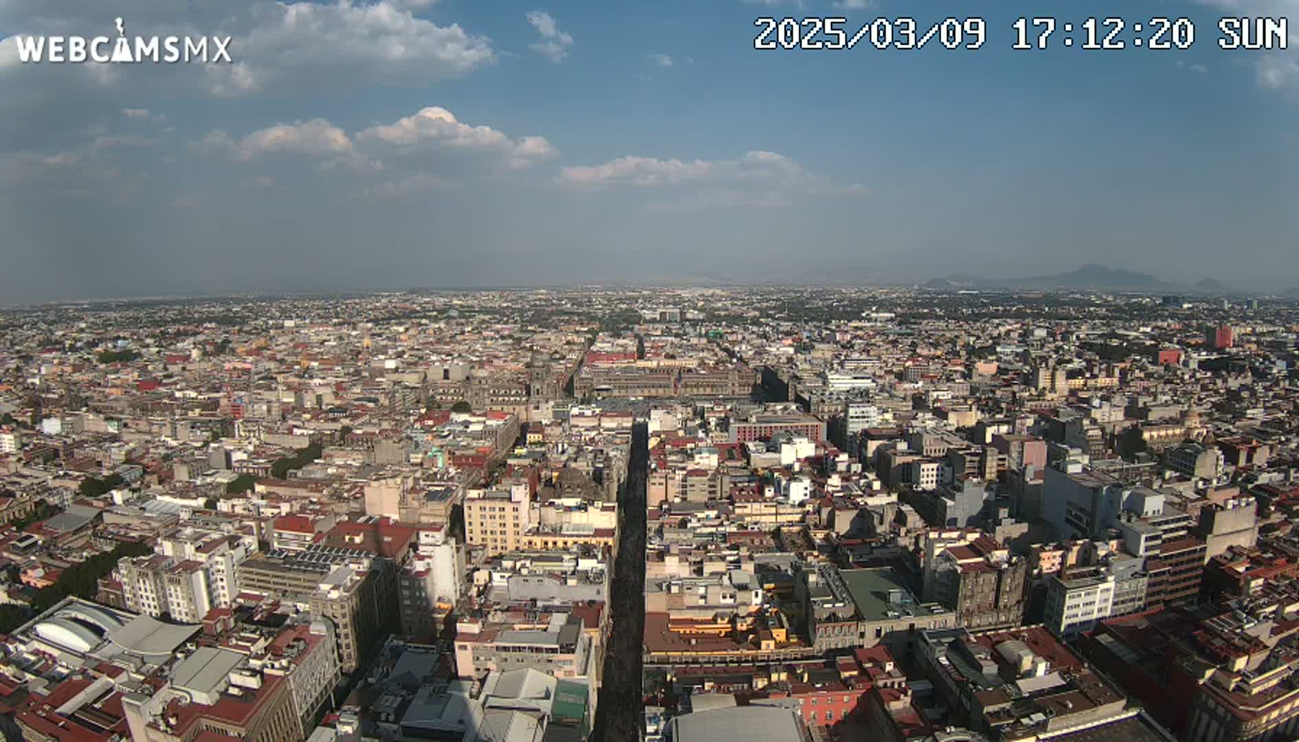 A high-angle, long shot of a sprawling city on a partly sunny day with some scattered clouds.