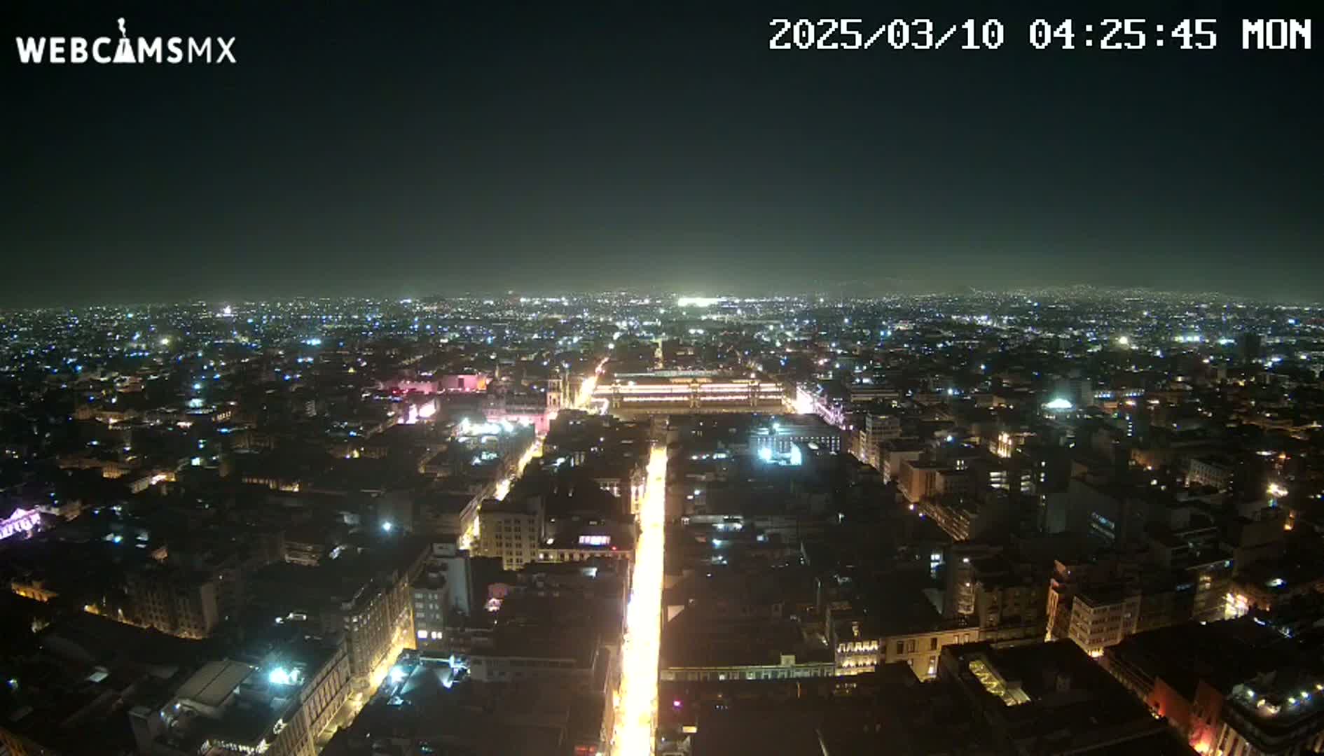 A nighttime aerial view of a brightly lit city with a long, illuminated street running through its center under a clear, dark sky.