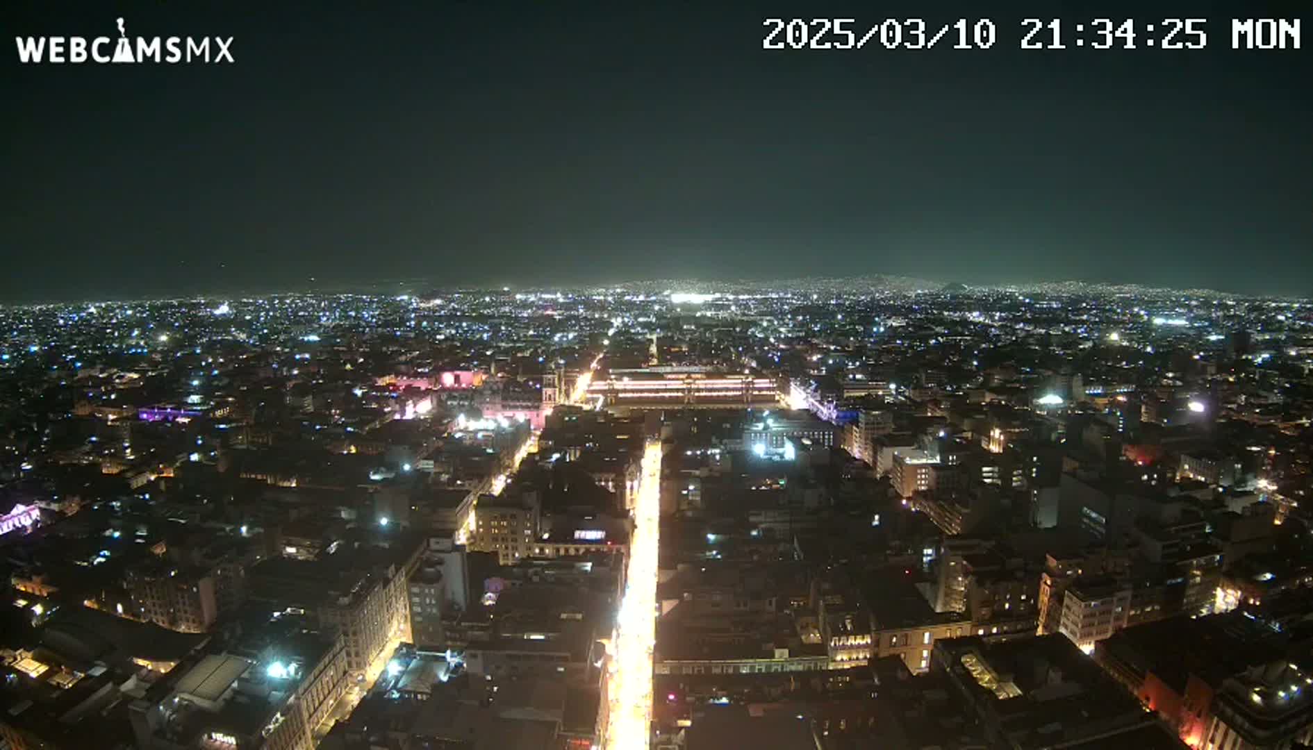 A nighttime aerial view of a brightly lit city sprawling across a dark landscape under a clear sky.