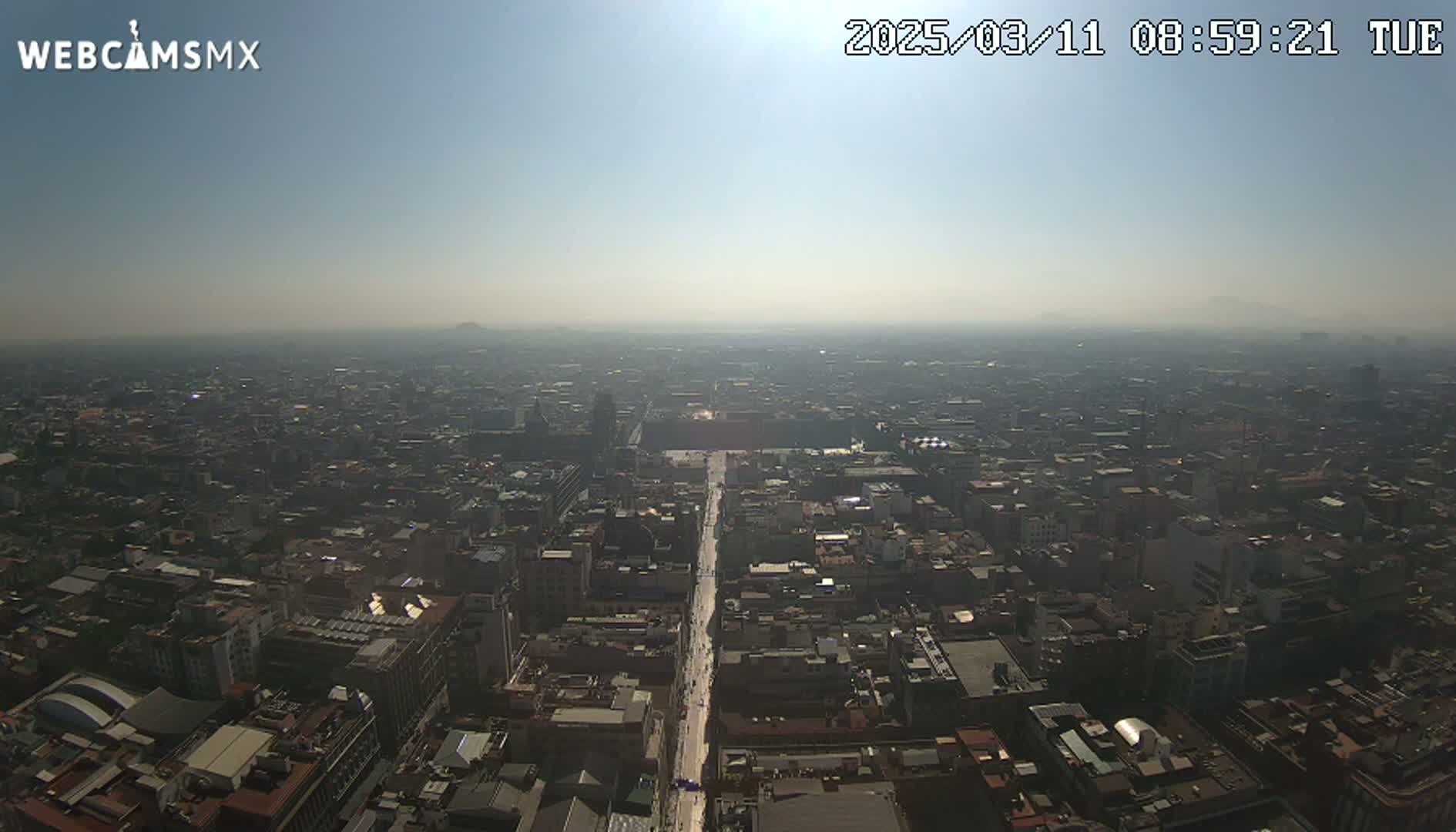 A hazy, sunny day reveals a sprawling cityscape with a long, straight avenue cutting through its center.