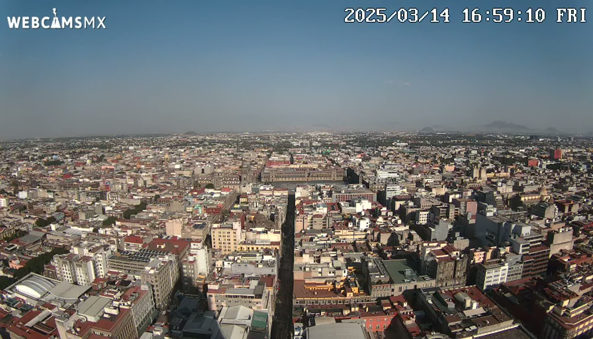 A high-angle, long shot on a clear day shows a sprawling cityscape of densely packed buildings extending to the horizon, with a single wide street cutting through the center.