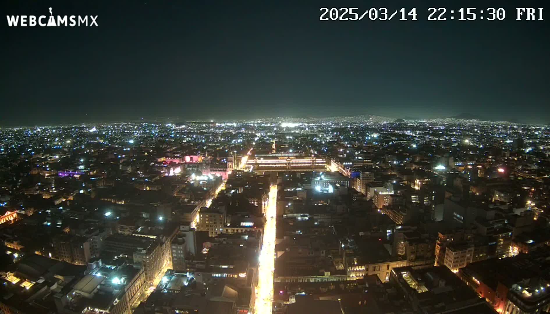 A nighttime aerial view shows a sprawling city illuminated by countless lights, with a brightly lit street running through the center.