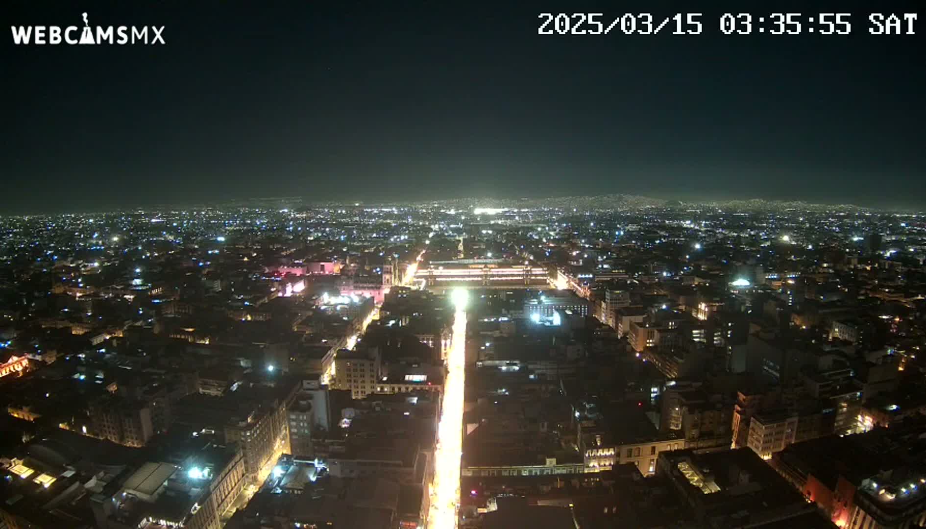 A brightly lit city at night is viewed from above, extending to a dark horizon under a clear sky.