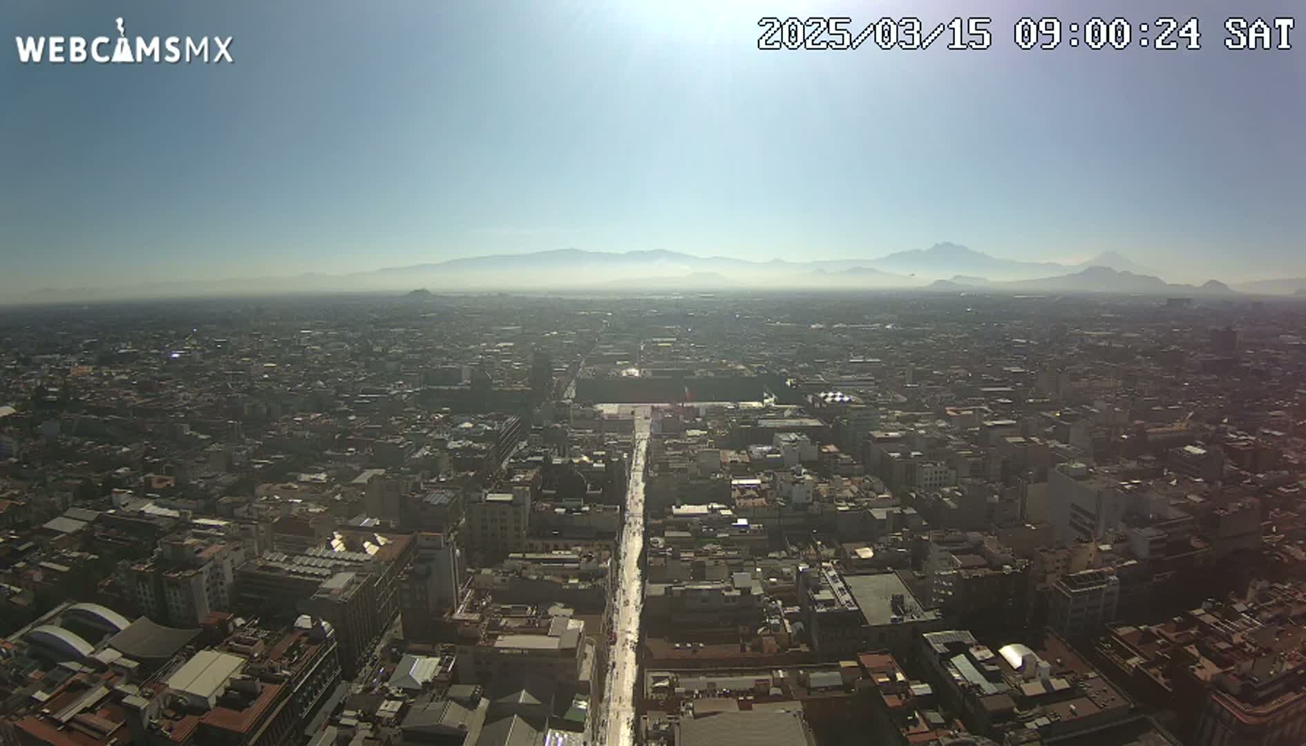 A hazy, sunny day reveals a sprawling cityscape stretching to distant mountains.