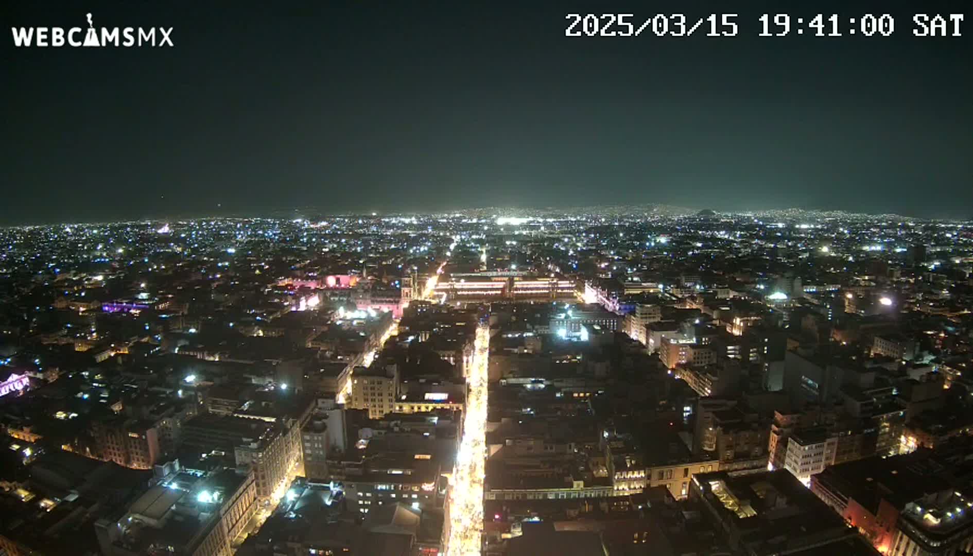 A nighttime, aerial view shows a brightly lit city sprawling across a wide area under a clear, dark sky.