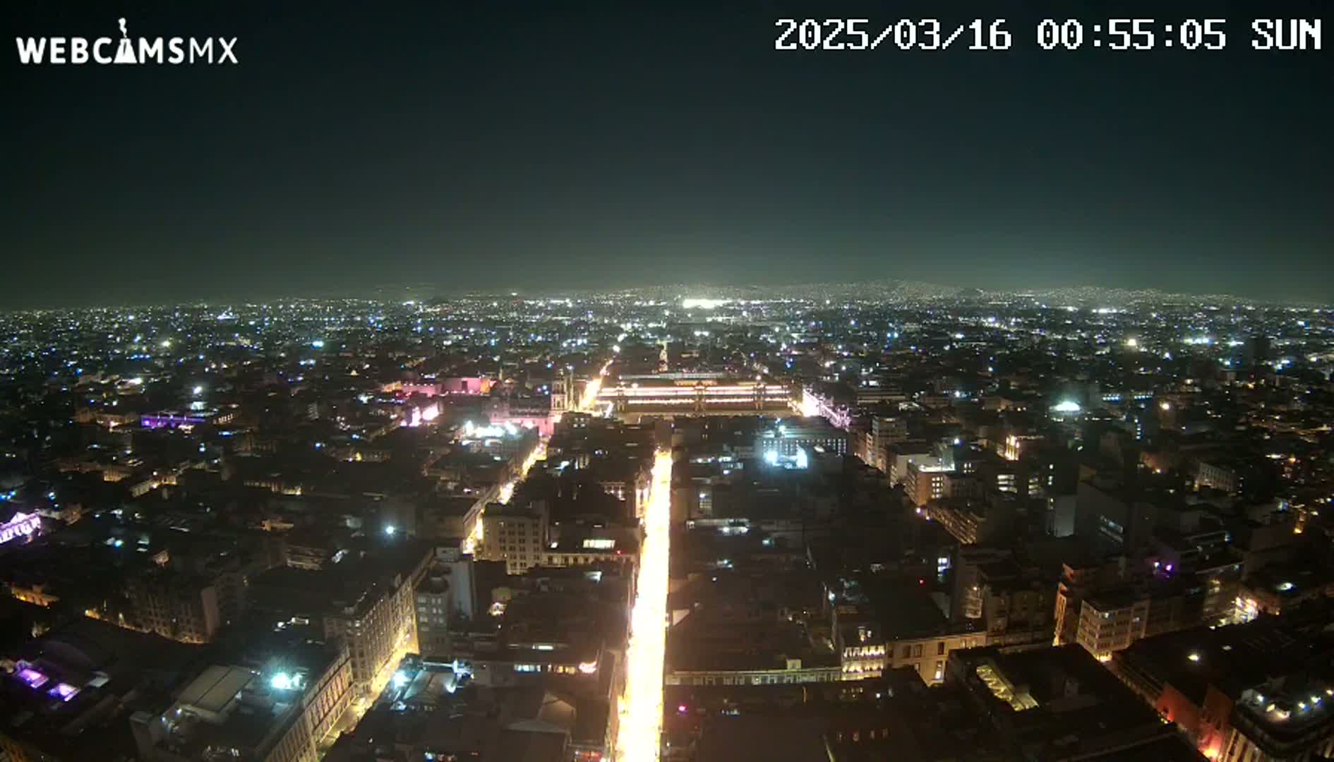A brightly lit city at night is seen from an aerial perspective, under a clear, dark sky.