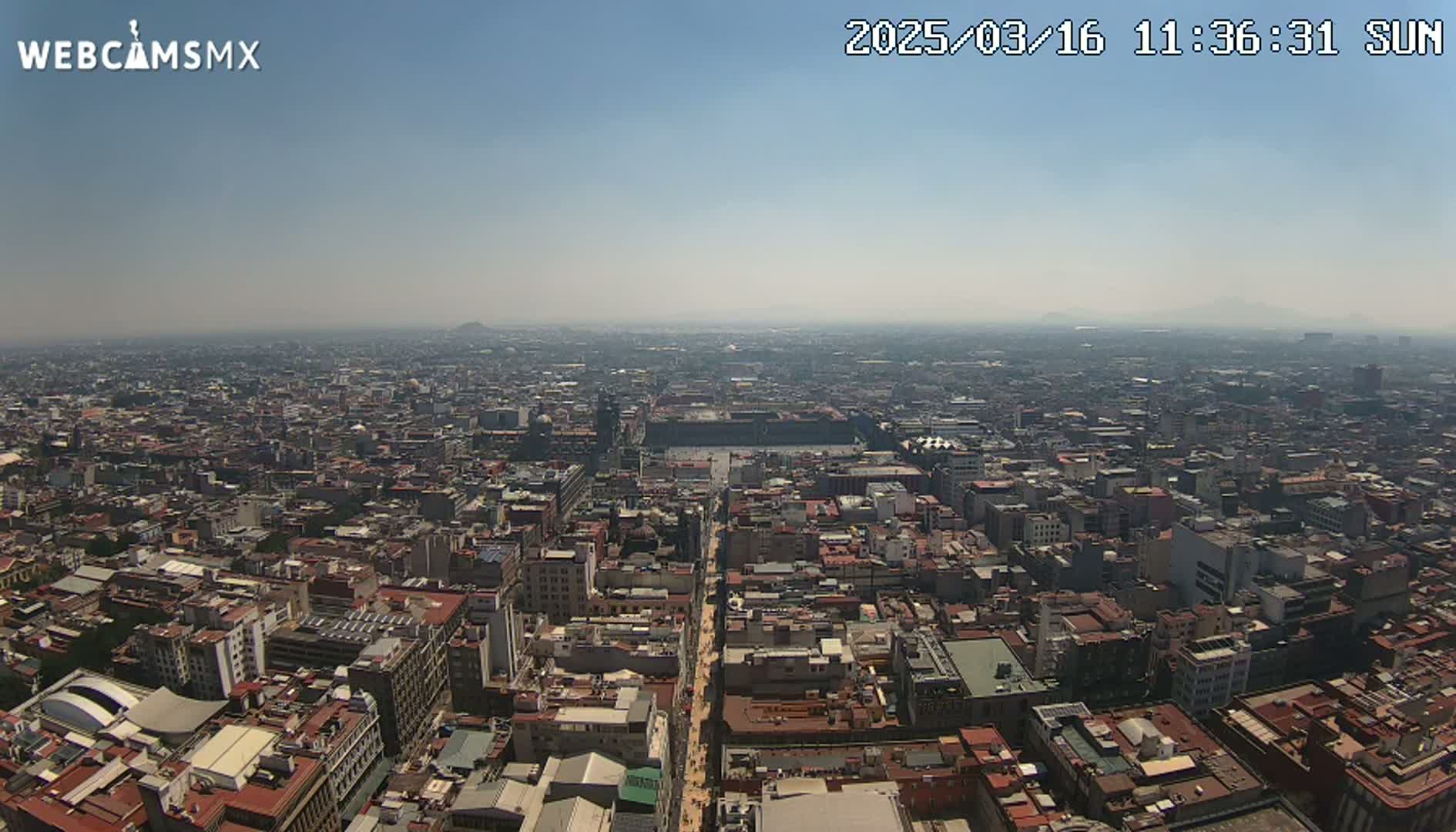 A hazy, sunny day overlooks a sprawling cityscape, with a large plaza visible in the center.