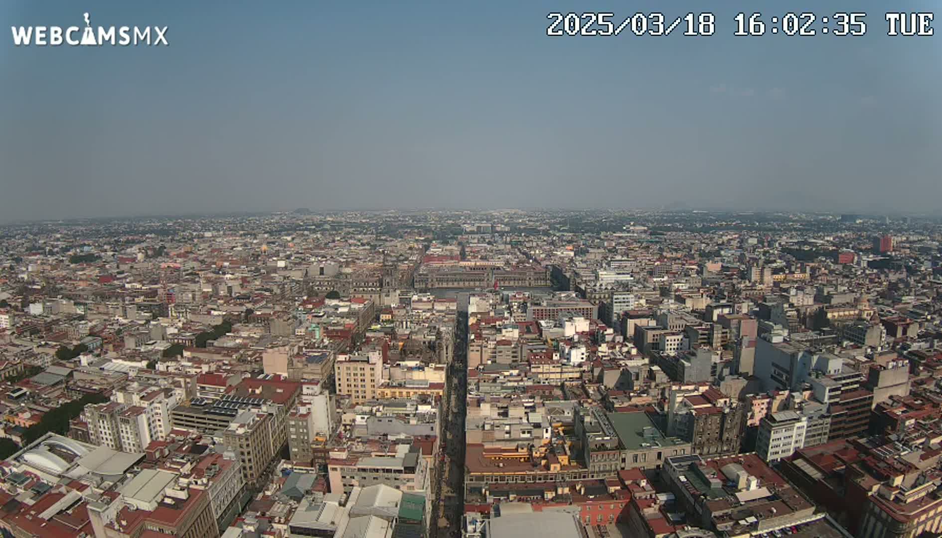 A hazy, high-angle view shows a sprawling cityscape extending to the horizon under a clear sky.