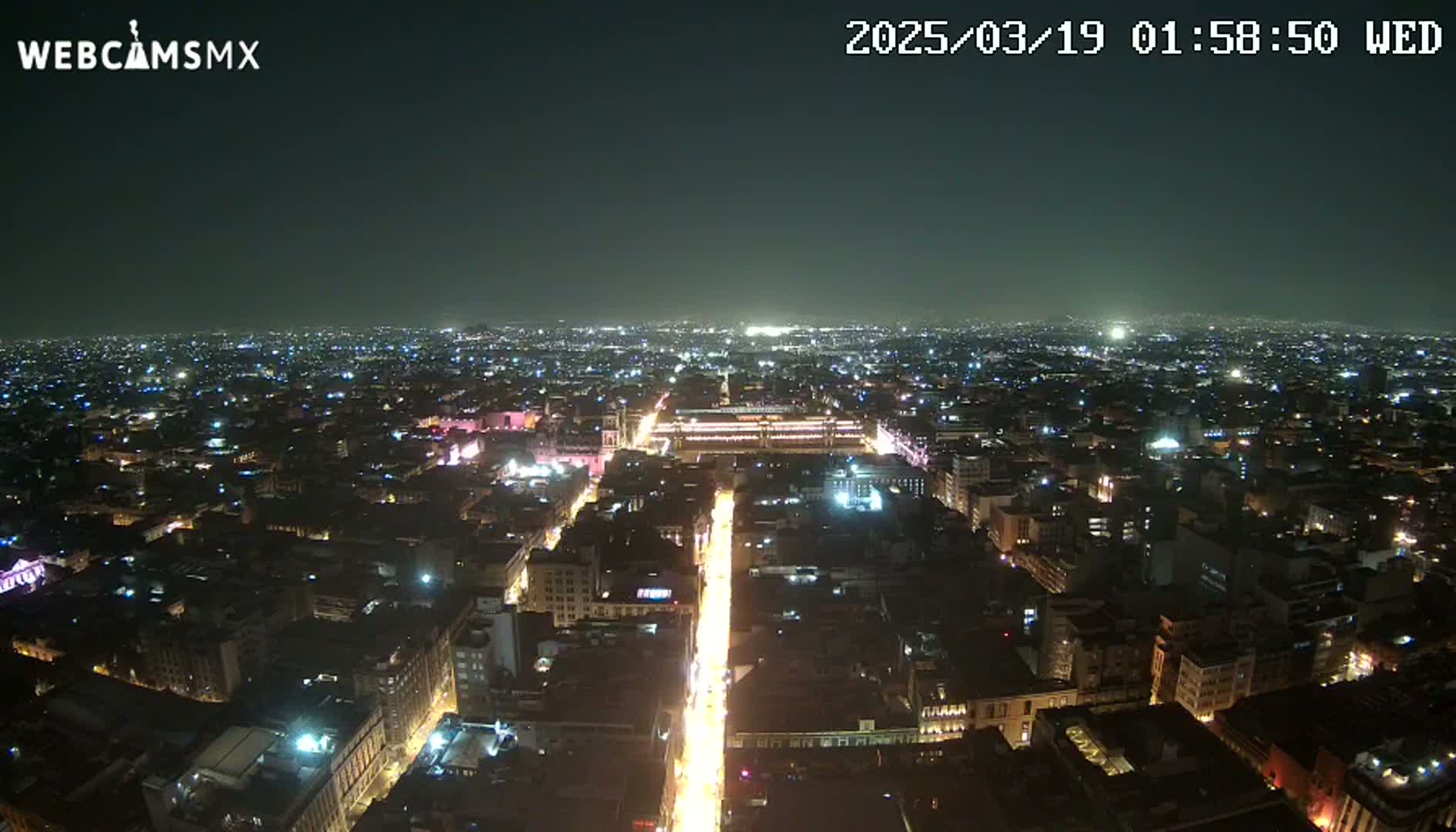 A nighttime aerial view shows a brightly lit city sprawling under a clear, dark sky.
