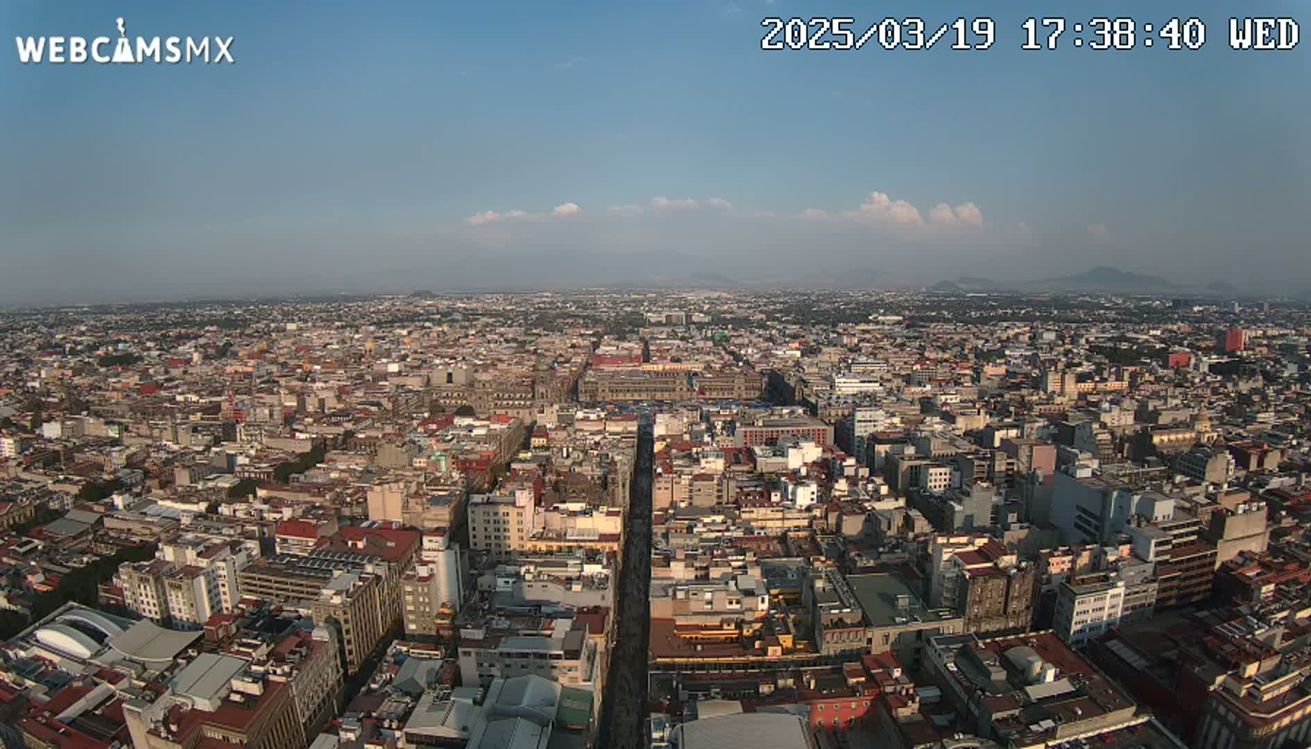 A high-angle, long shot of a sprawling city on a partly sunny day with a few clouds in the sky.