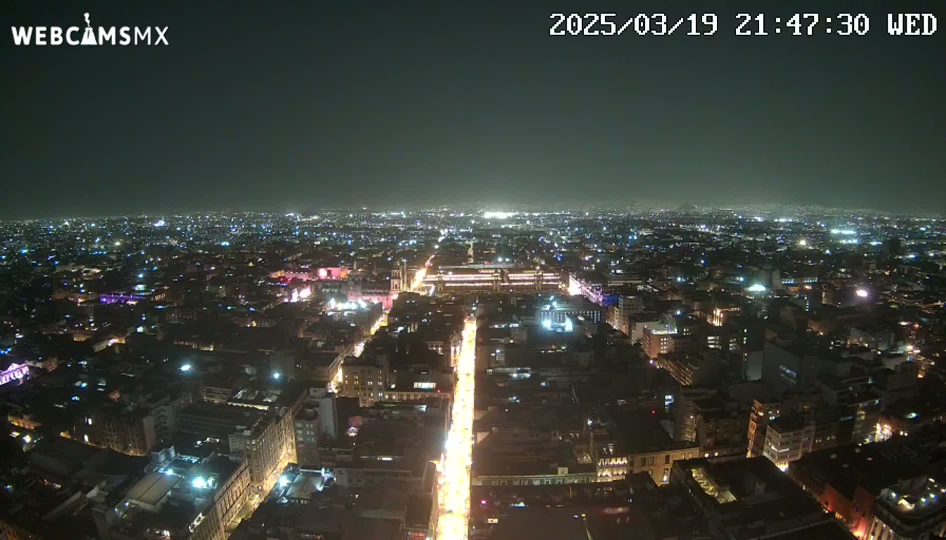 A nighttime aerial view of a city with brightly lit streets and buildings under a clear, dark sky.