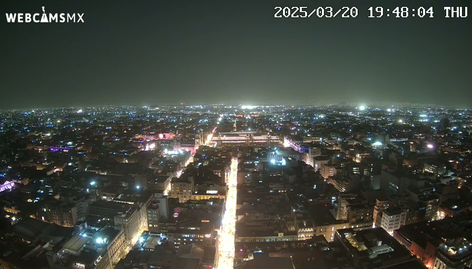 A nighttime aerial view shows a brightly lit city sprawling under a dark, clear sky.