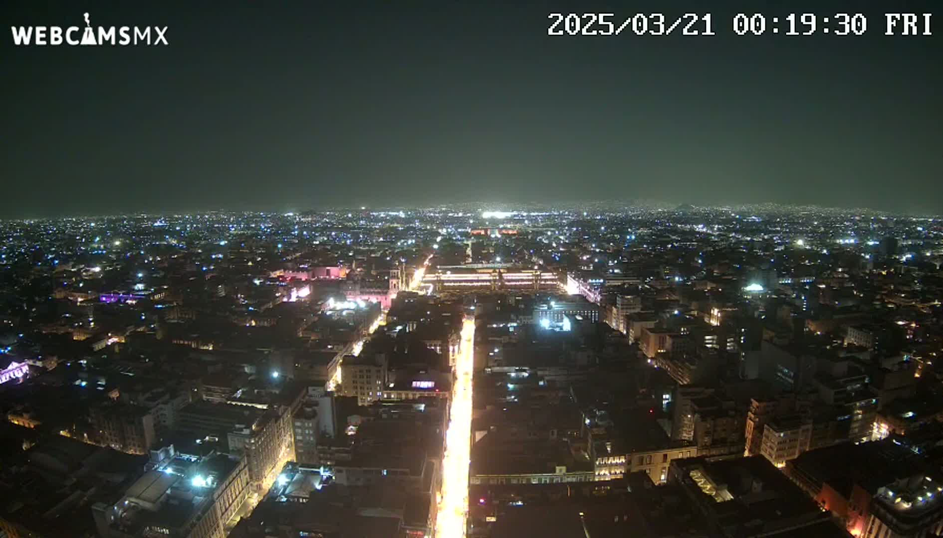 A nighttime aerial view of a brightly lit city with a long, illuminated street running through its center under a clear, dark sky.