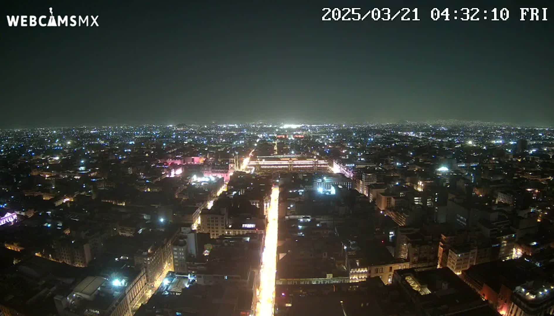 A nighttime aerial view shows a city illuminated by streetlights, with a long, brightly lit street running through the center.