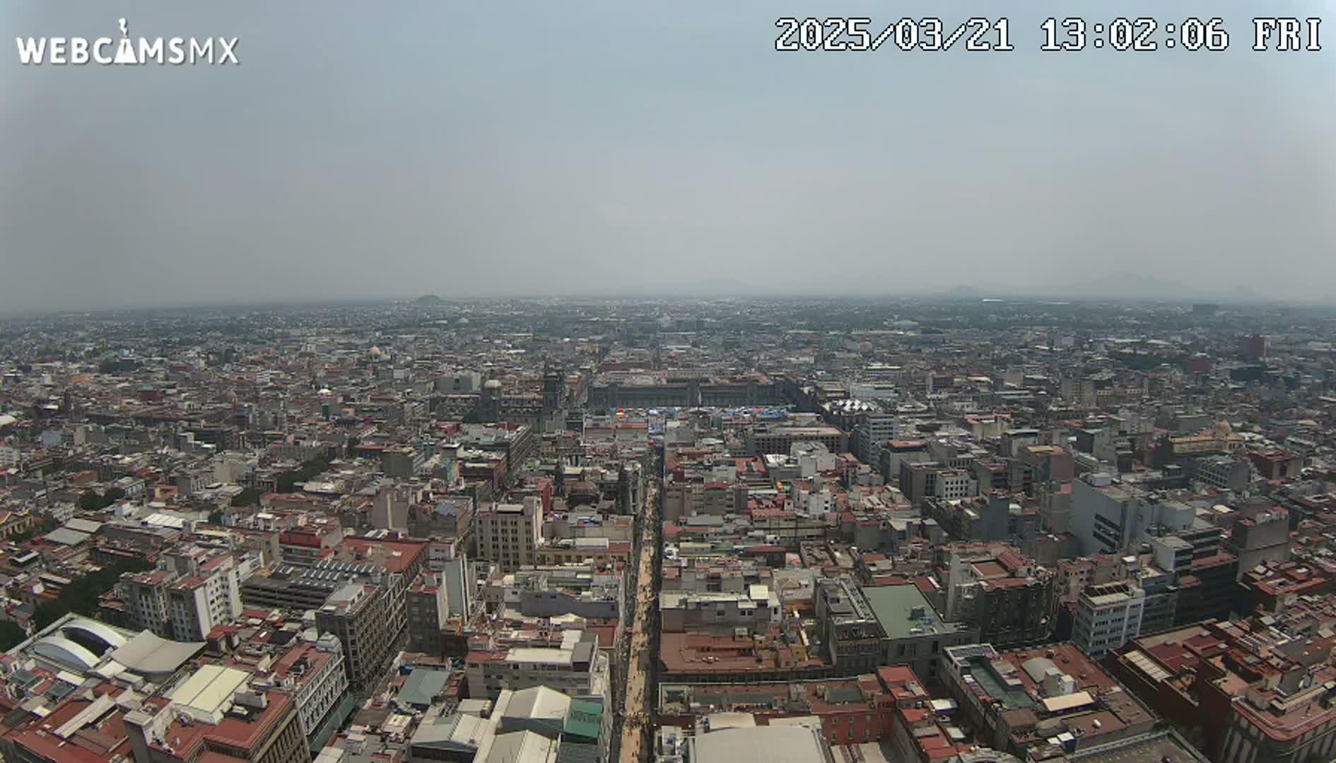 A hazy, high-angle view shows a vast cityscape stretching to the horizon under a light-grey sky.