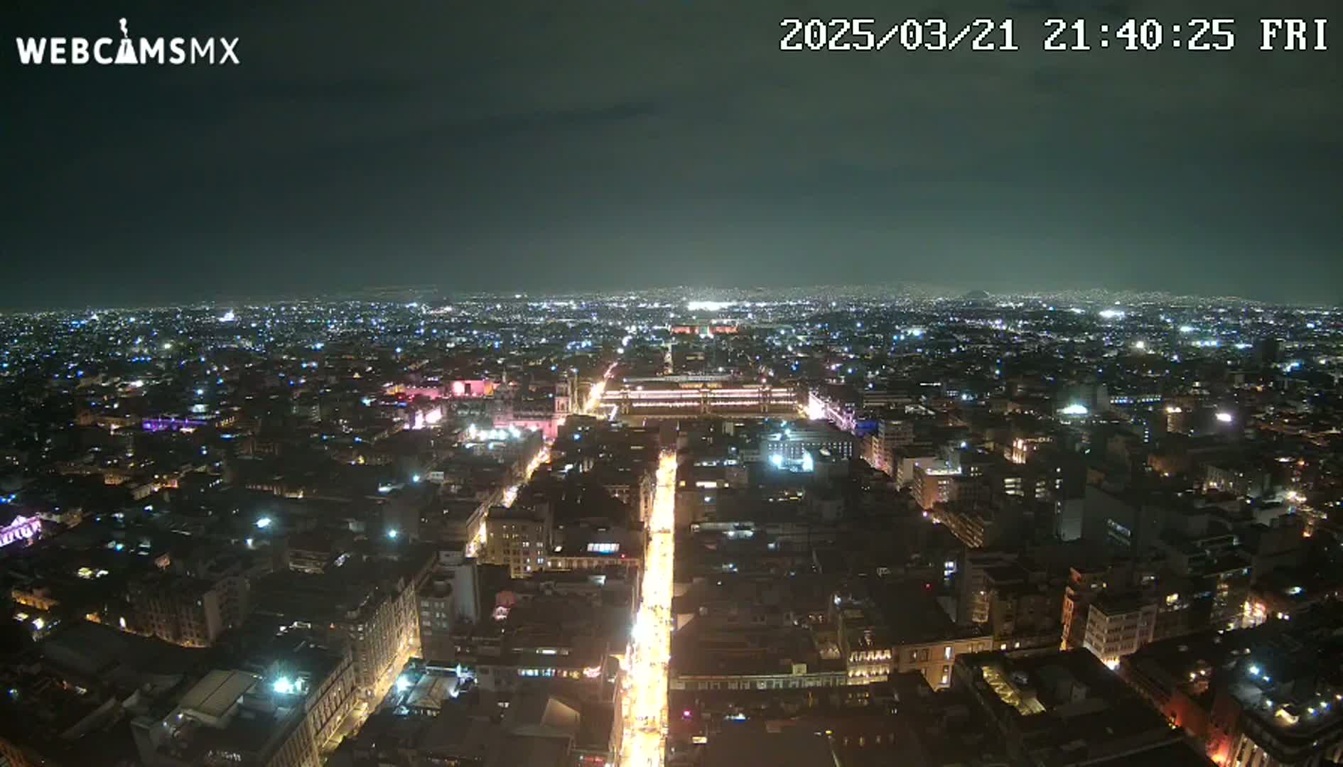 A brightly lit city at night is seen from a high vantage point under a clear, dark sky.