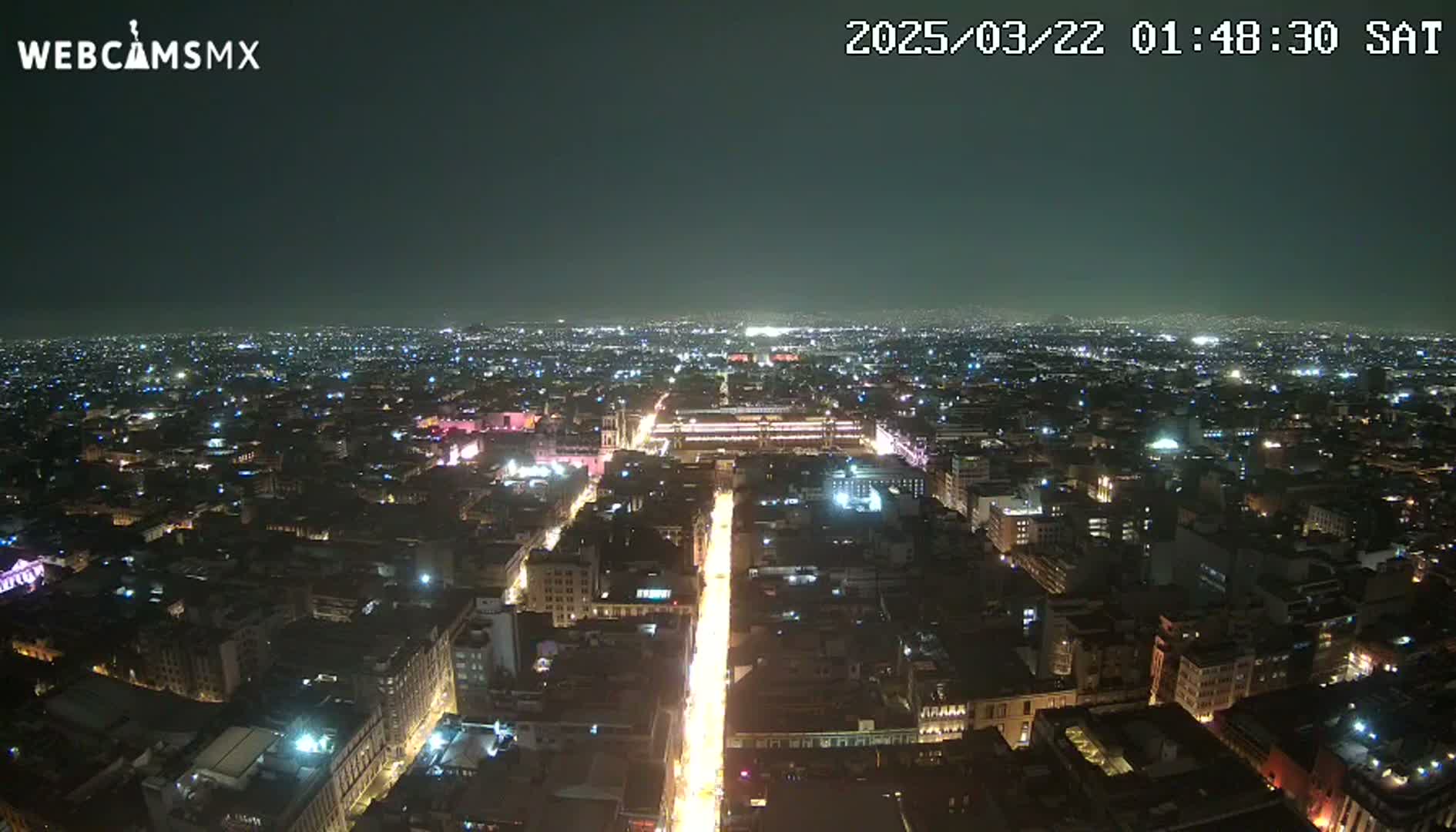 A nighttime aerial view shows a sprawling city illuminated by streetlights and building lights under a clear, dark sky.