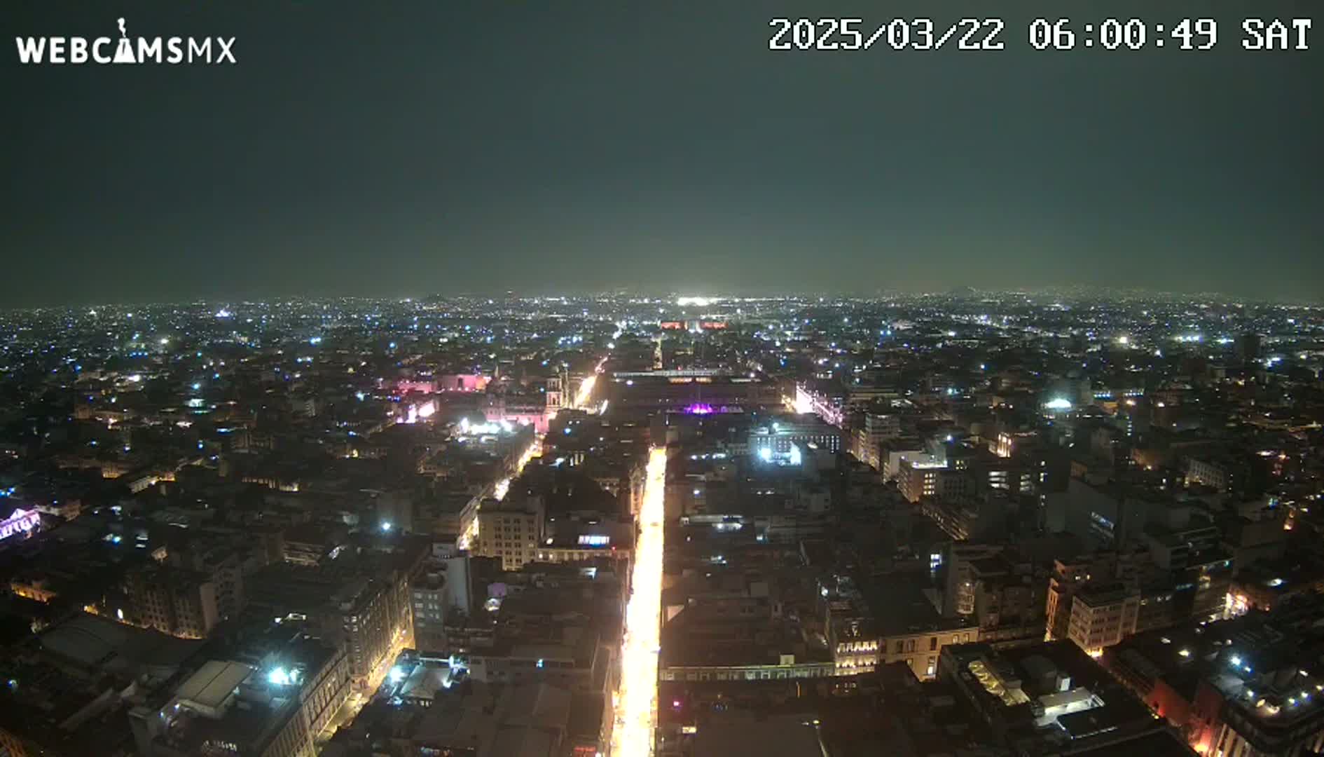 A nighttime aerial view of a city with a brightly lit street running through its center under a clear, dark sky.