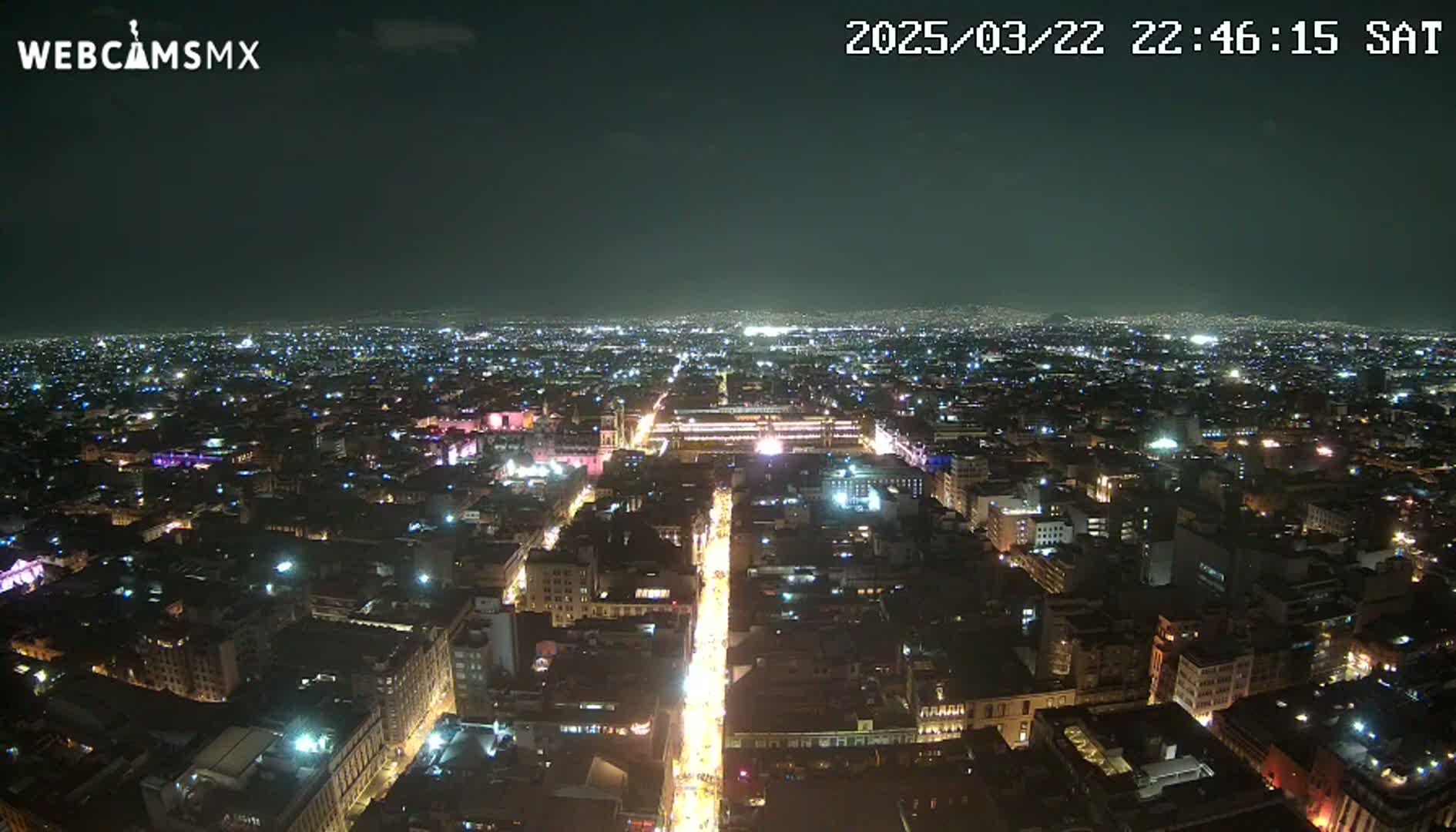 A nighttime, aerial view shows a brightly lit city sprawling across a dark landscape under a clear sky.