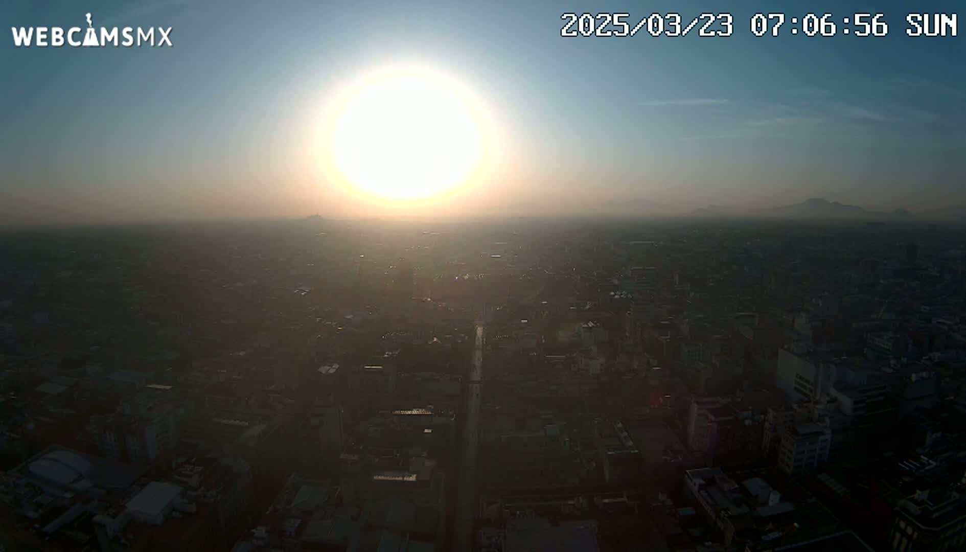 A hazy sunrise illuminates a sprawling city, with distant mountains barely visible on the horizon.