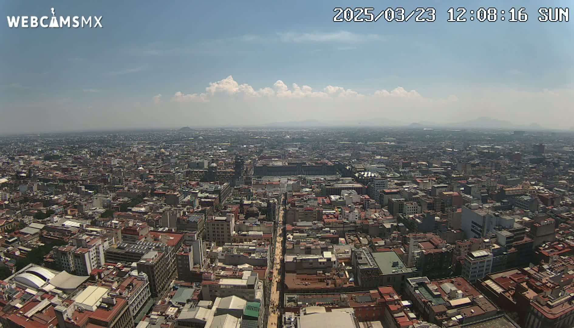 A high-angle, long shot of a sprawling city on a partly sunny day with some scattered clouds.