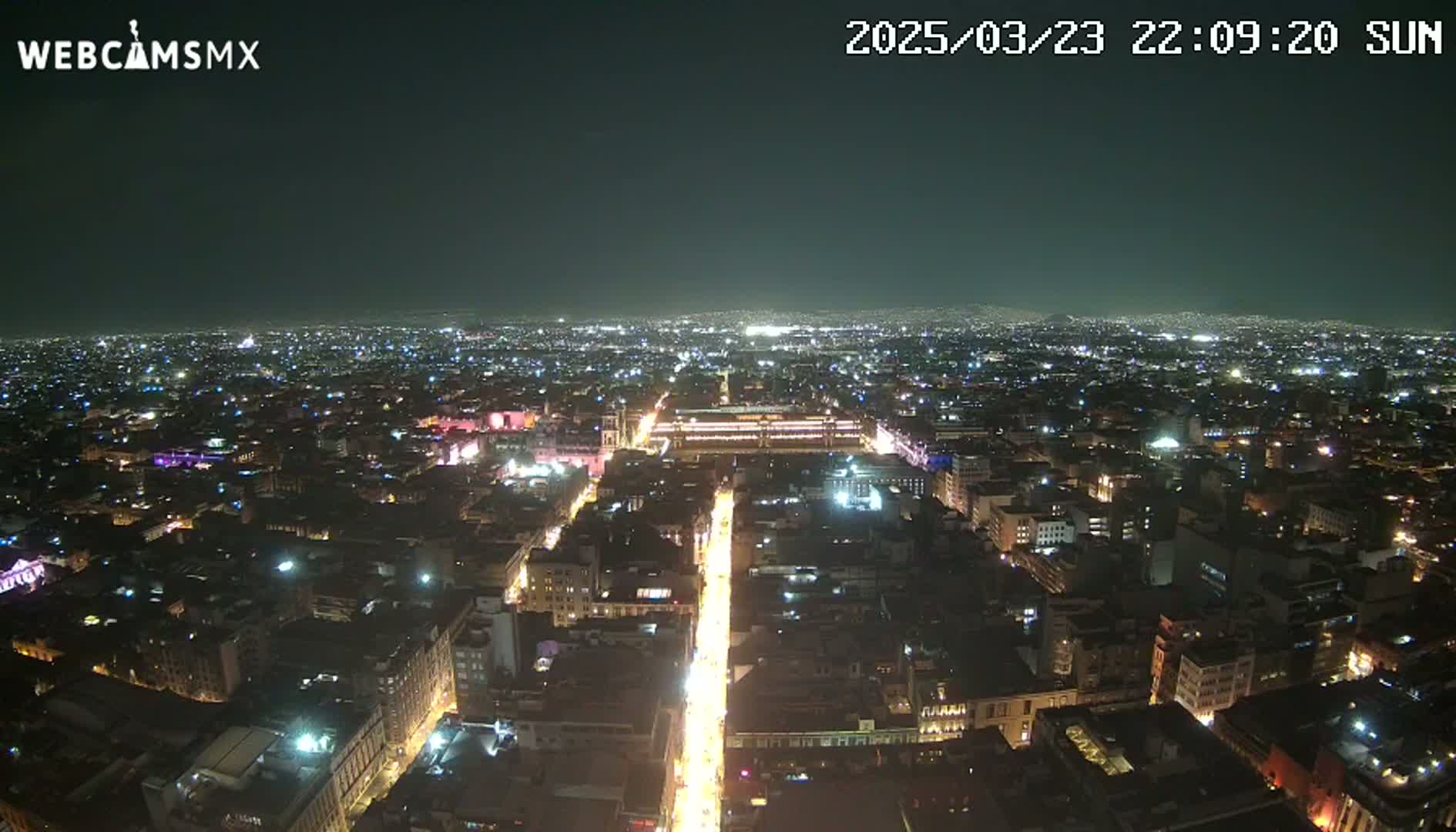 A brightly lit city at night is viewed from above, under a clear, dark sky.