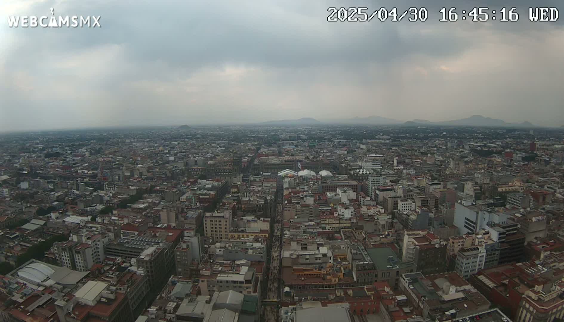 A sprawling cityscape under an overcast sky extends to distant mountains.