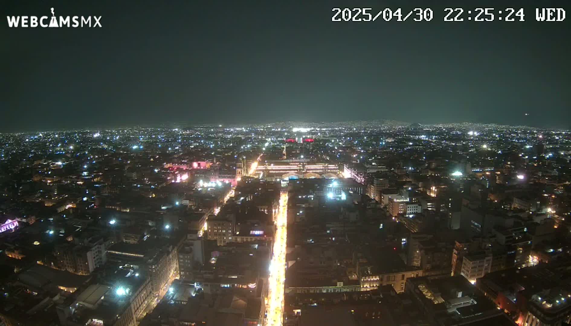 A nighttime aerial view of a brightly lit city, showing a long, illuminated street extending from the foreground into the distance.