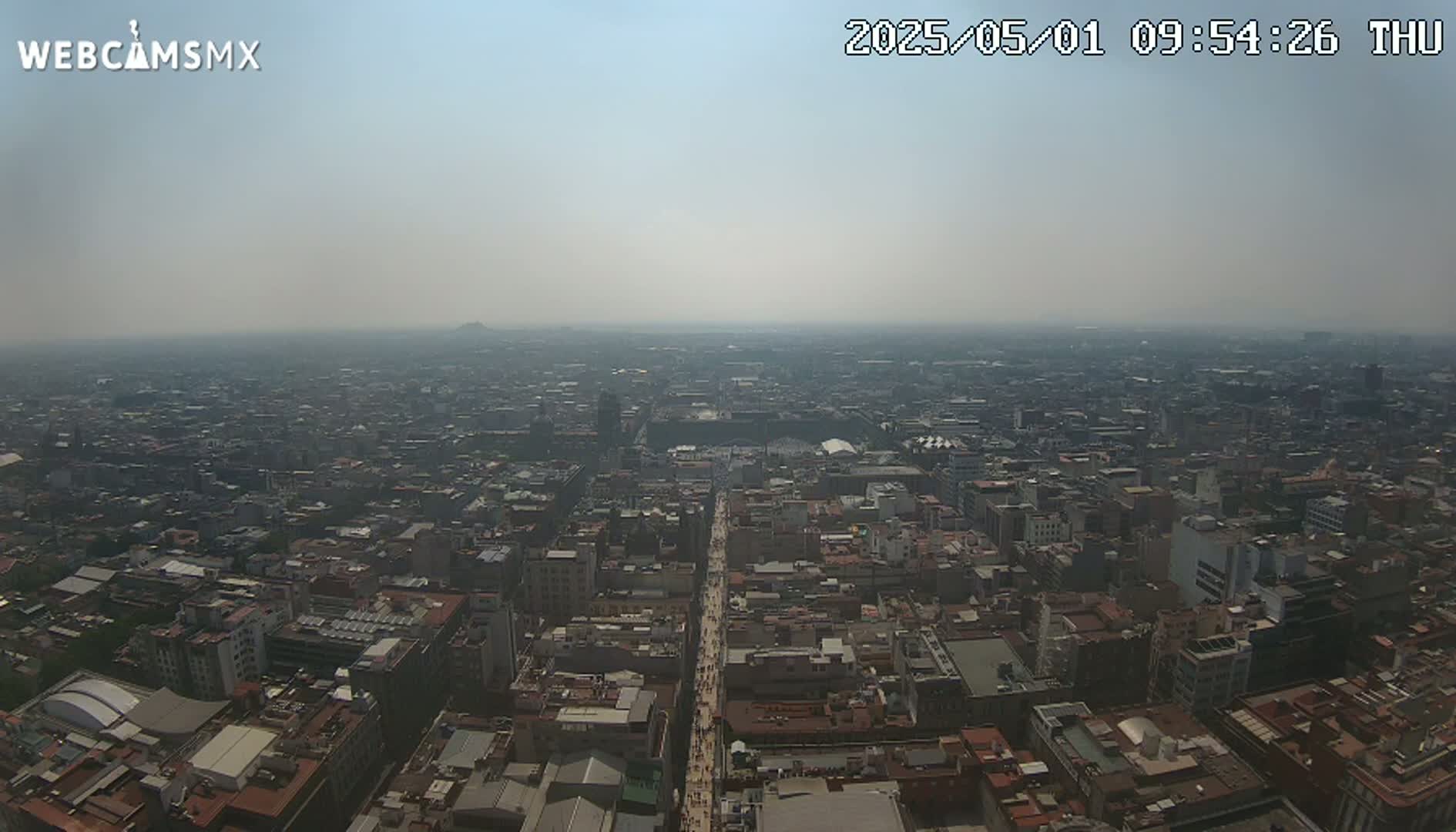A hazy, high-angle view shows a vast expanse of a city, with a long street or avenue cutting through its center.