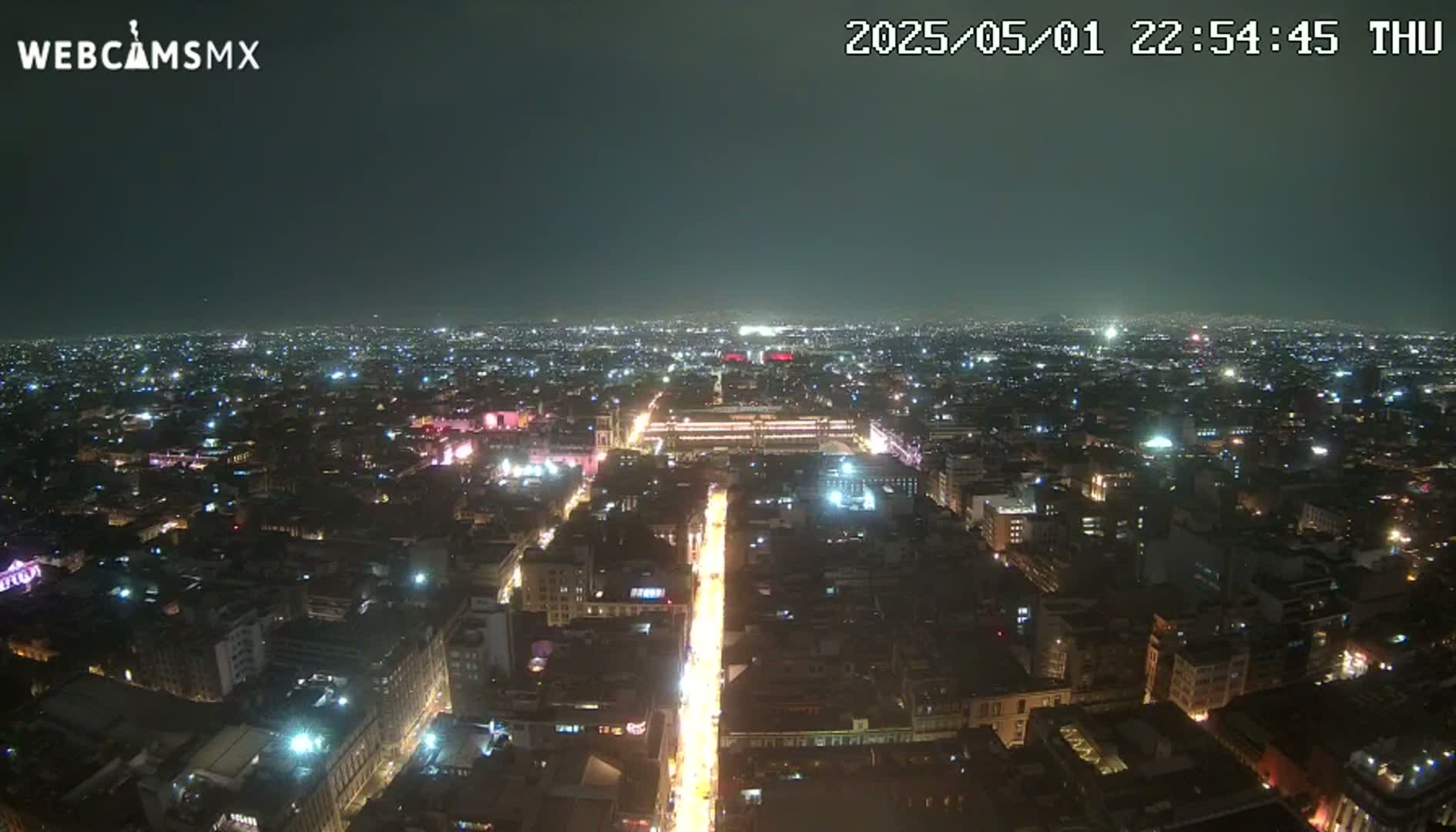 A nighttime aerial view shows a sprawling city with illuminated streets and buildings under a clear, dark sky.