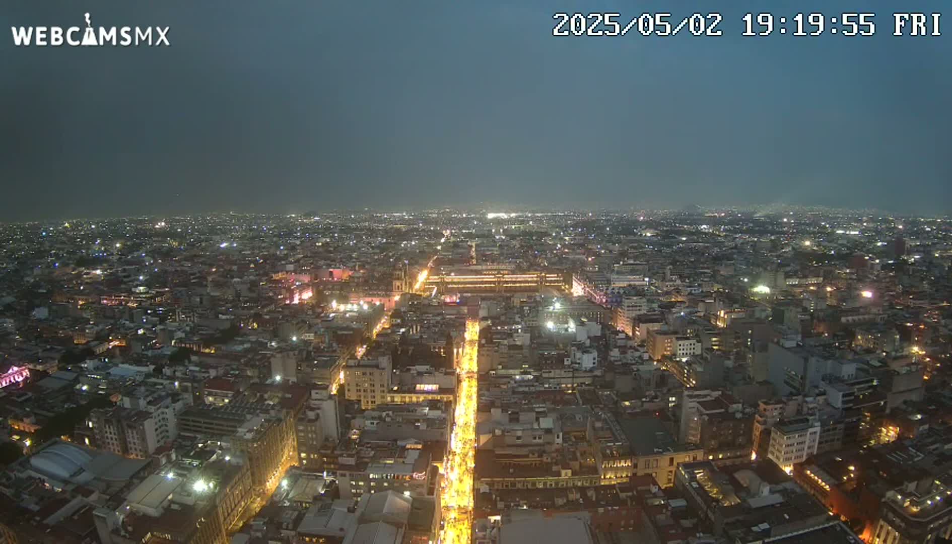 A nighttime aerial view of a sprawling city with brightly lit streets and buildings under a dusky sky.