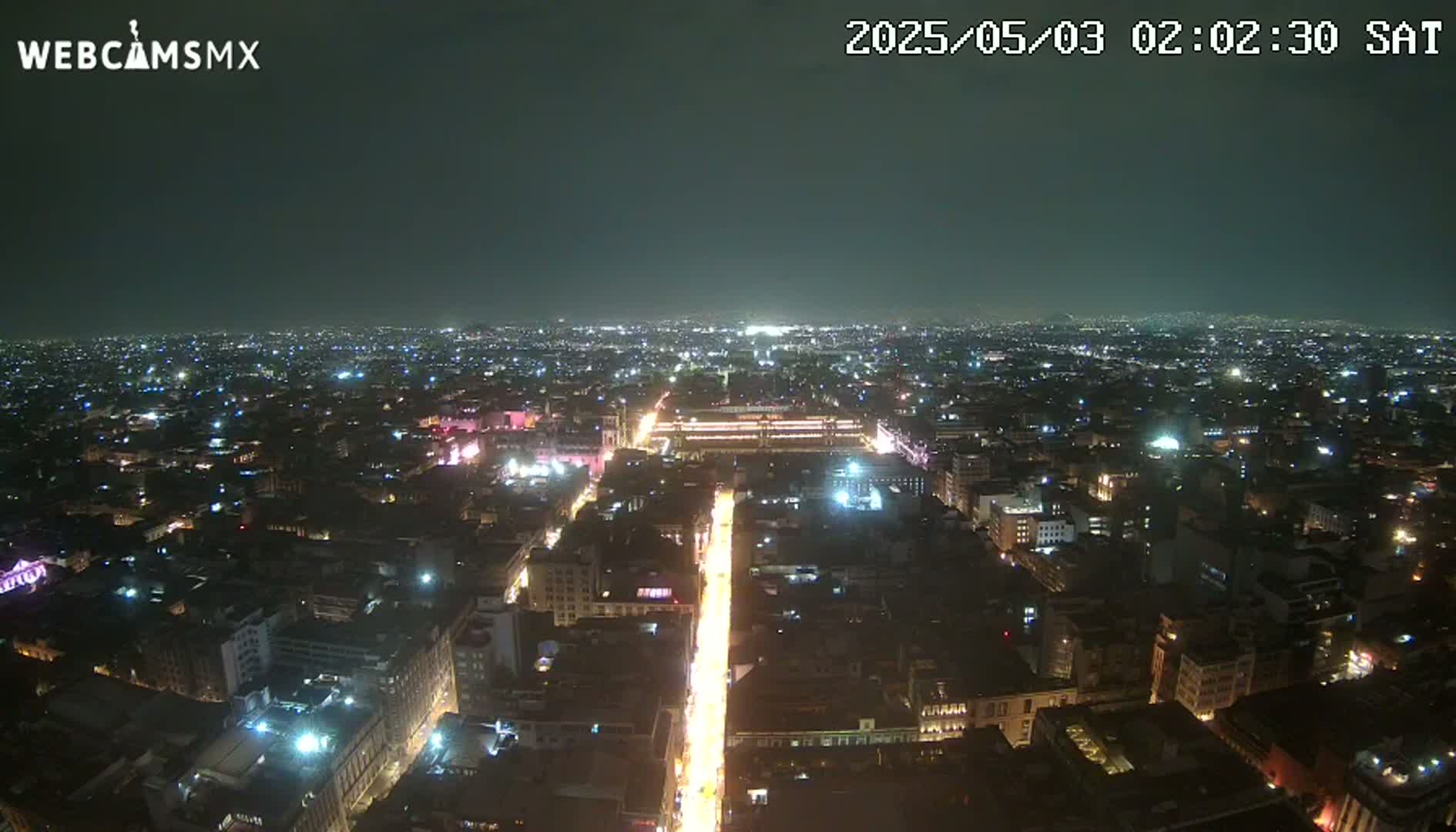 A brightly lit city at night is viewed from above, under a clear, dark sky.