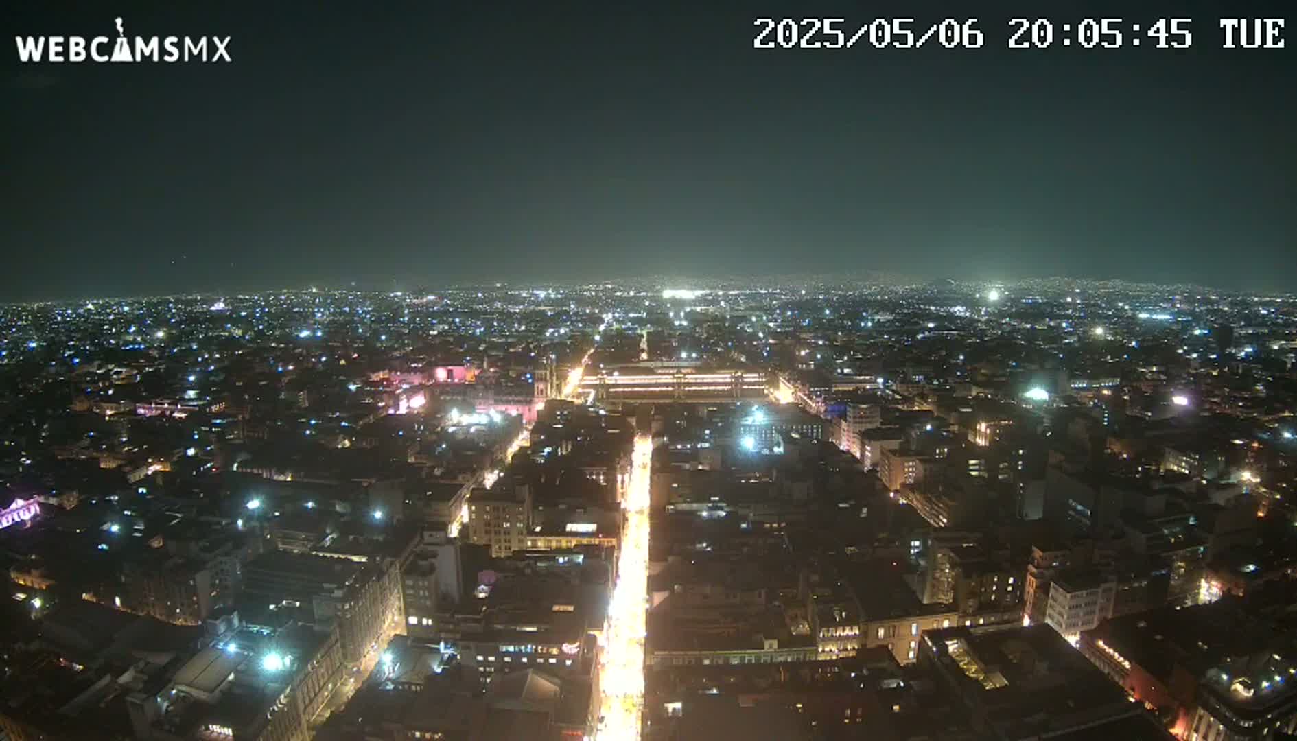 A nighttime aerial view of a sprawling city illuminated by countless lights, under a clear, dark sky.