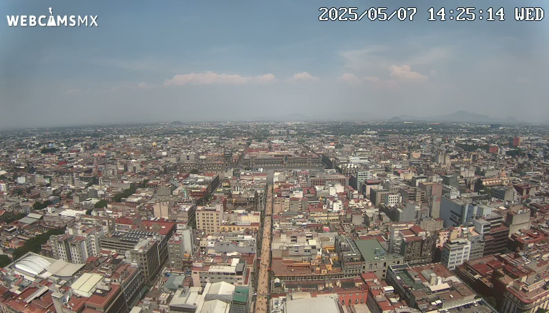 A high-angle, long shot on a partly cloudy day shows a sprawling cityscape with a wide avenue cutting through its center.