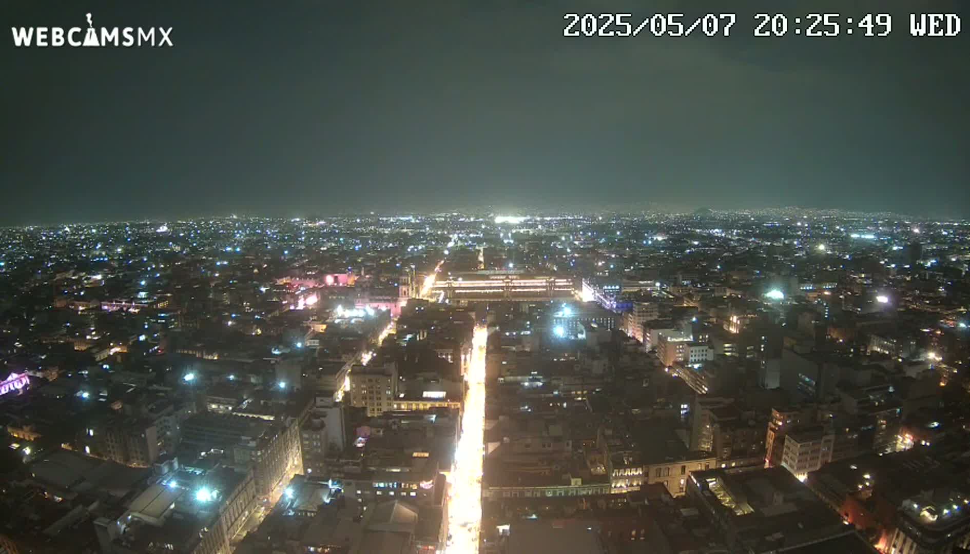 A nighttime, high-angle view shows a sprawling city illuminated by numerous streetlights and building lights under a clear, dark sky.